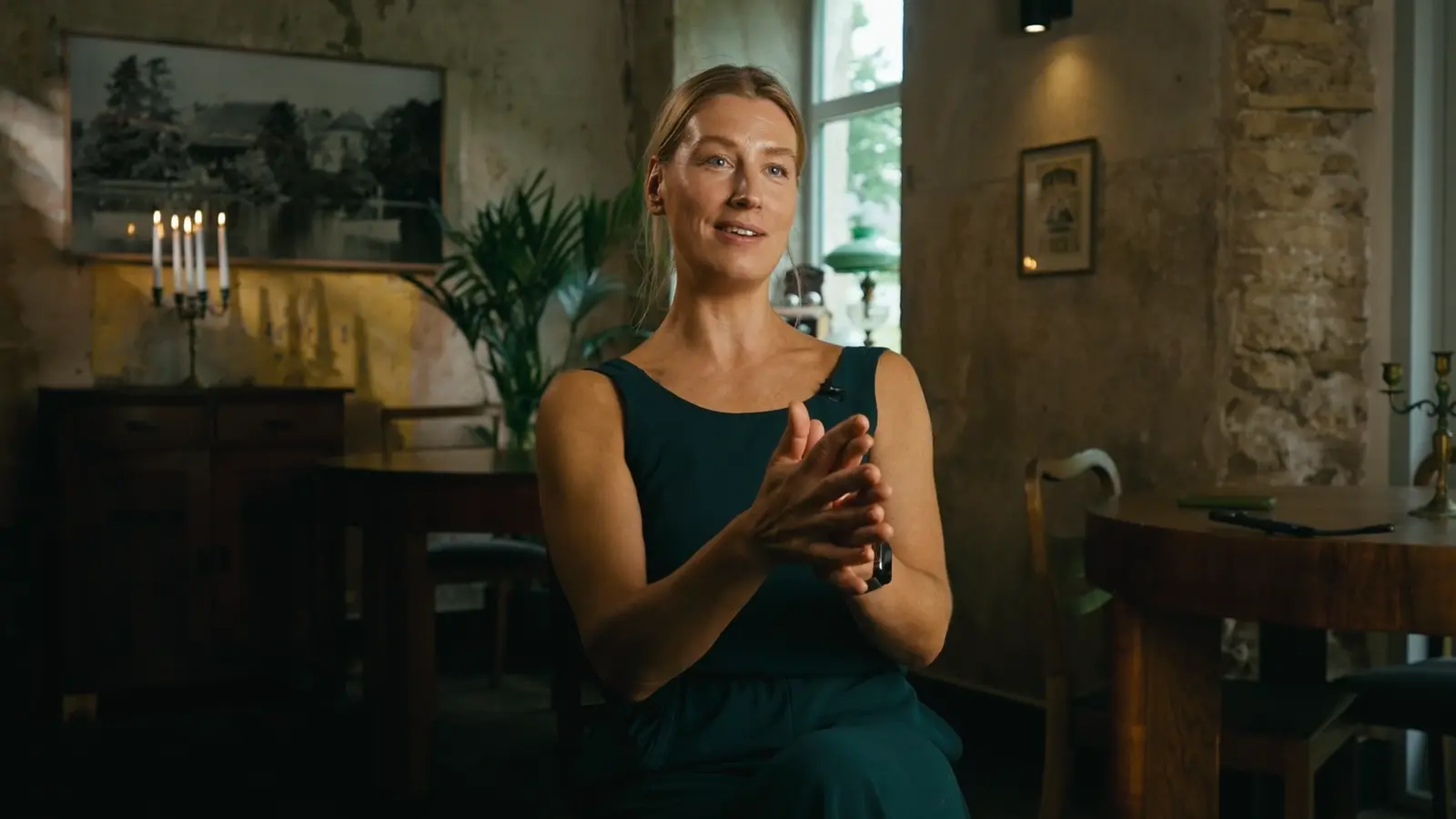 Woman in a green dress gesturing while being interviewed indoors