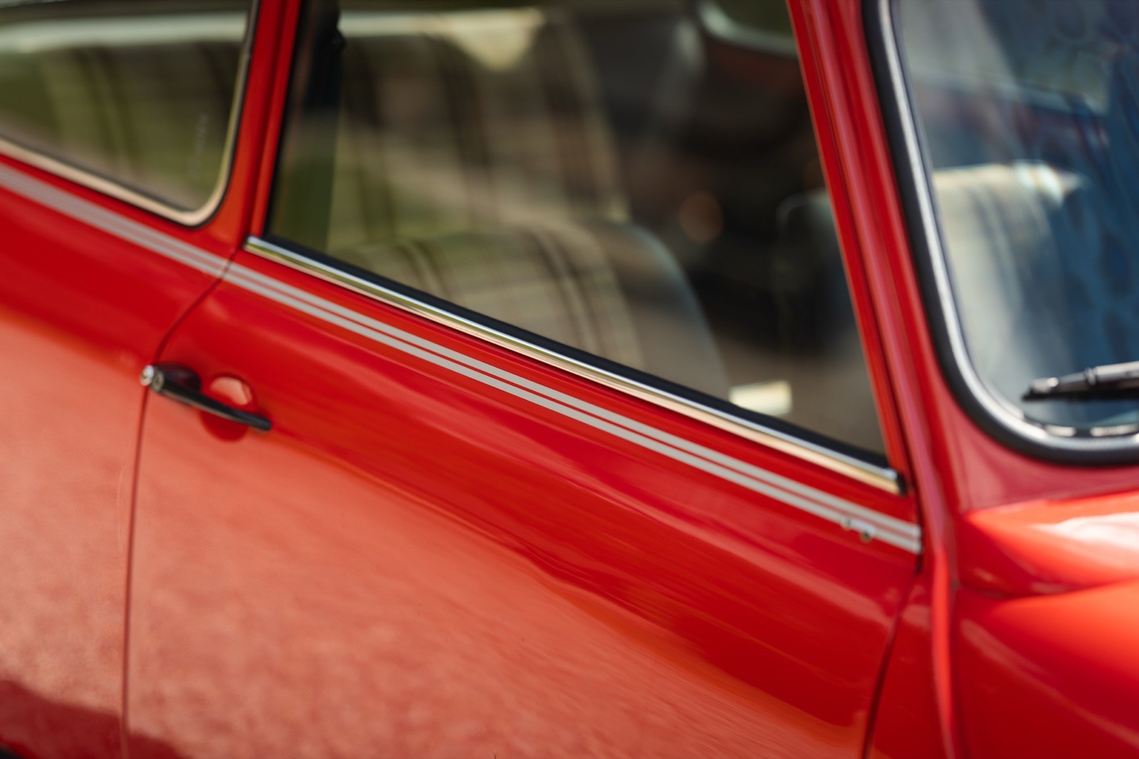 Close-up of a vintage red car's door, showing the handle and part of the window with a reflection.