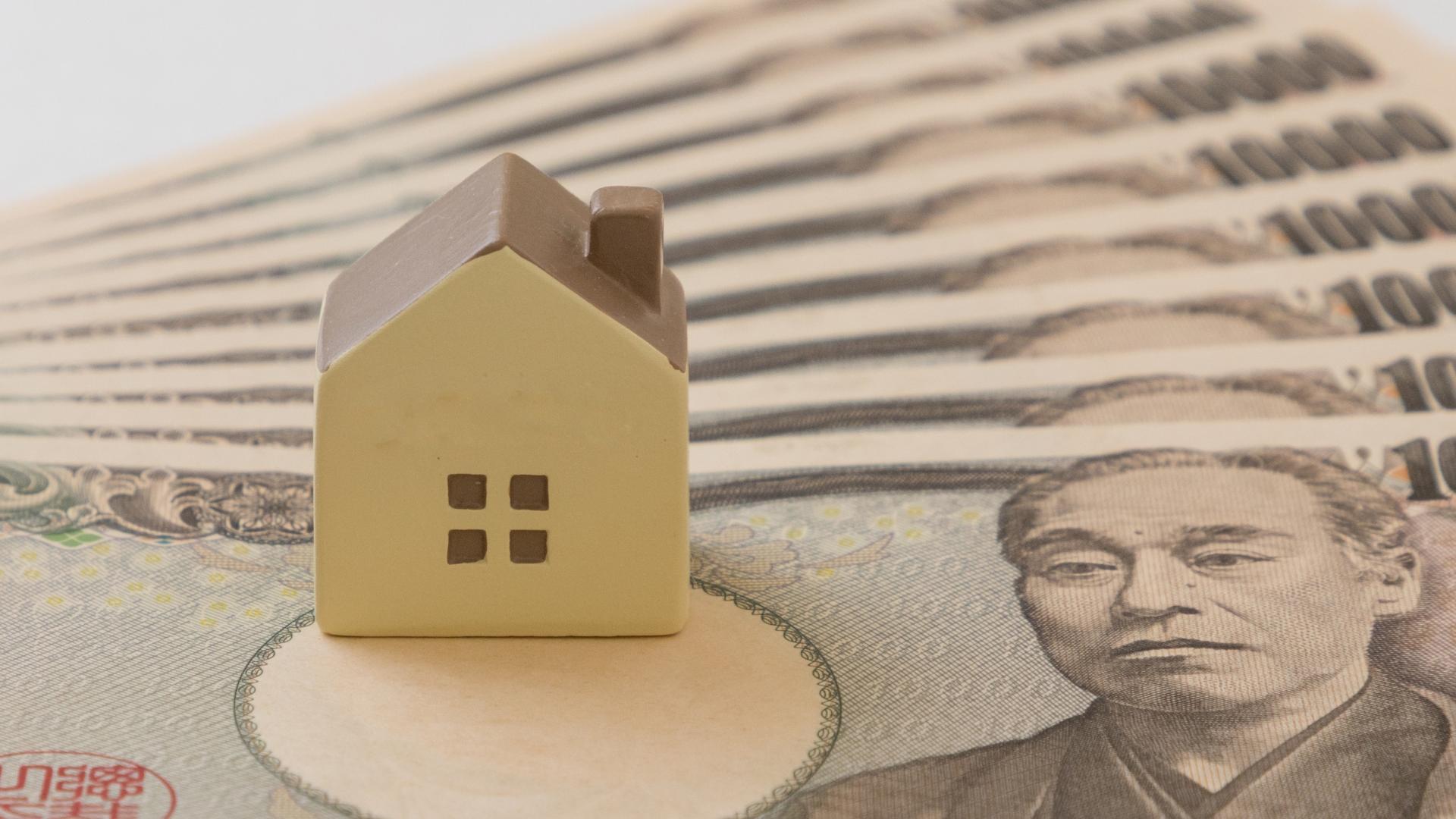 1万円札の上に置かれた小さな家の模型