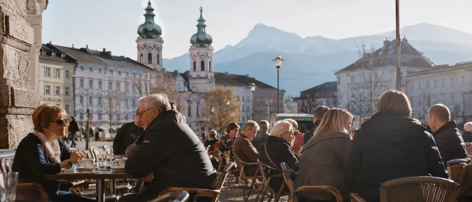 Mittelgroße österreichische Stadt mit Altstadtcafé, Barocktürmen und Alpen im Hintergrund