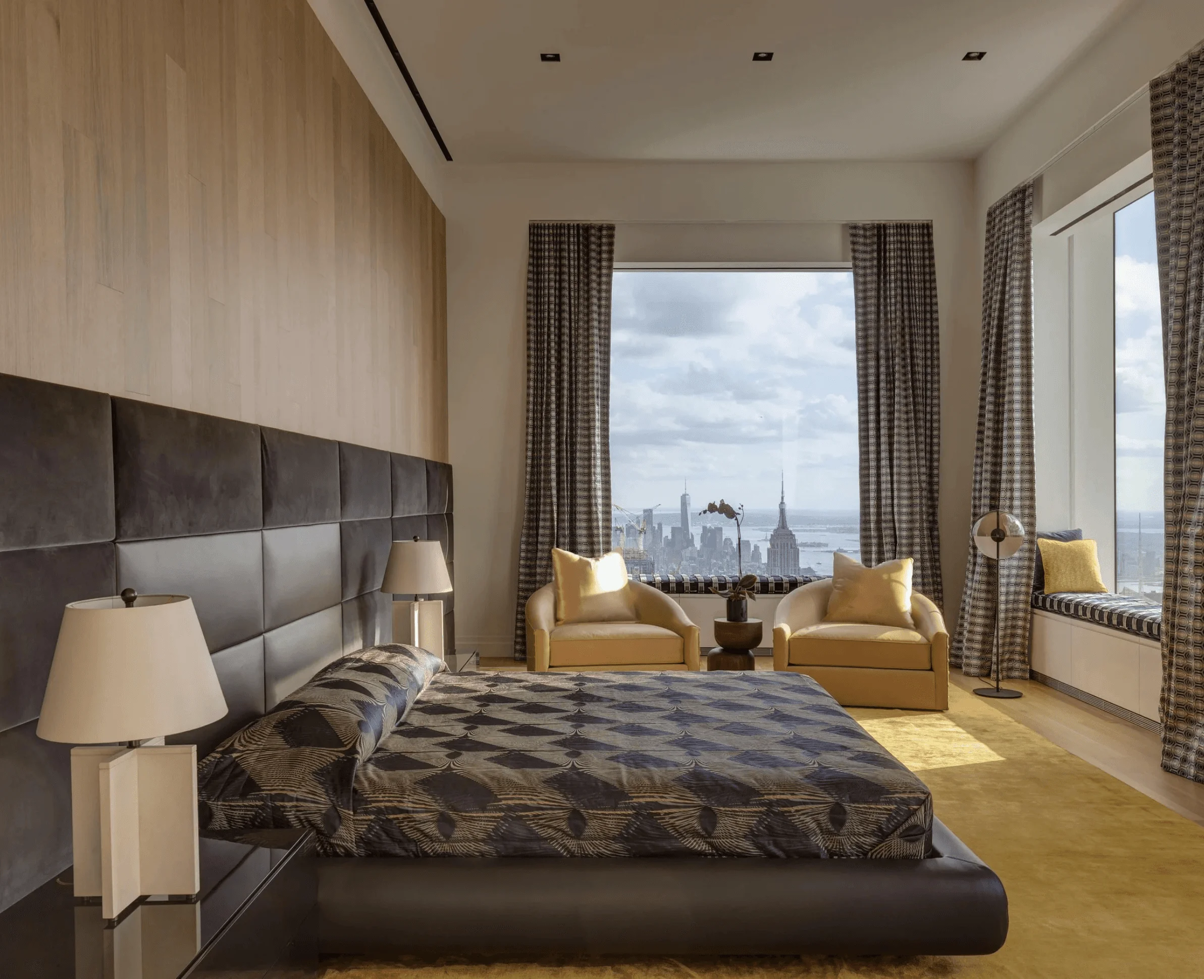 Silk curtains and a saffron rug bring warmth to this Deco-style primary bedroom's upholstered headboard