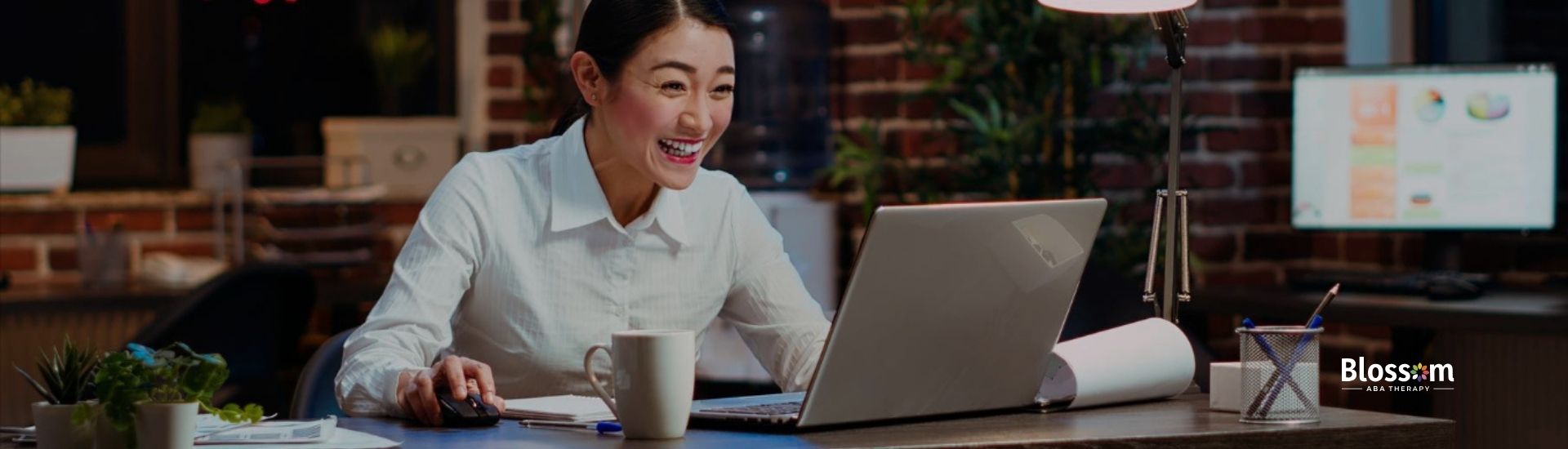 Autistic woman in a white blouse smiling and working on a laptop in a modern office.