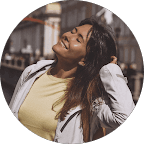 Portrait of a young man with wavy dark hair and a trimmed beard in a white sweater, soft light on a neutral background.