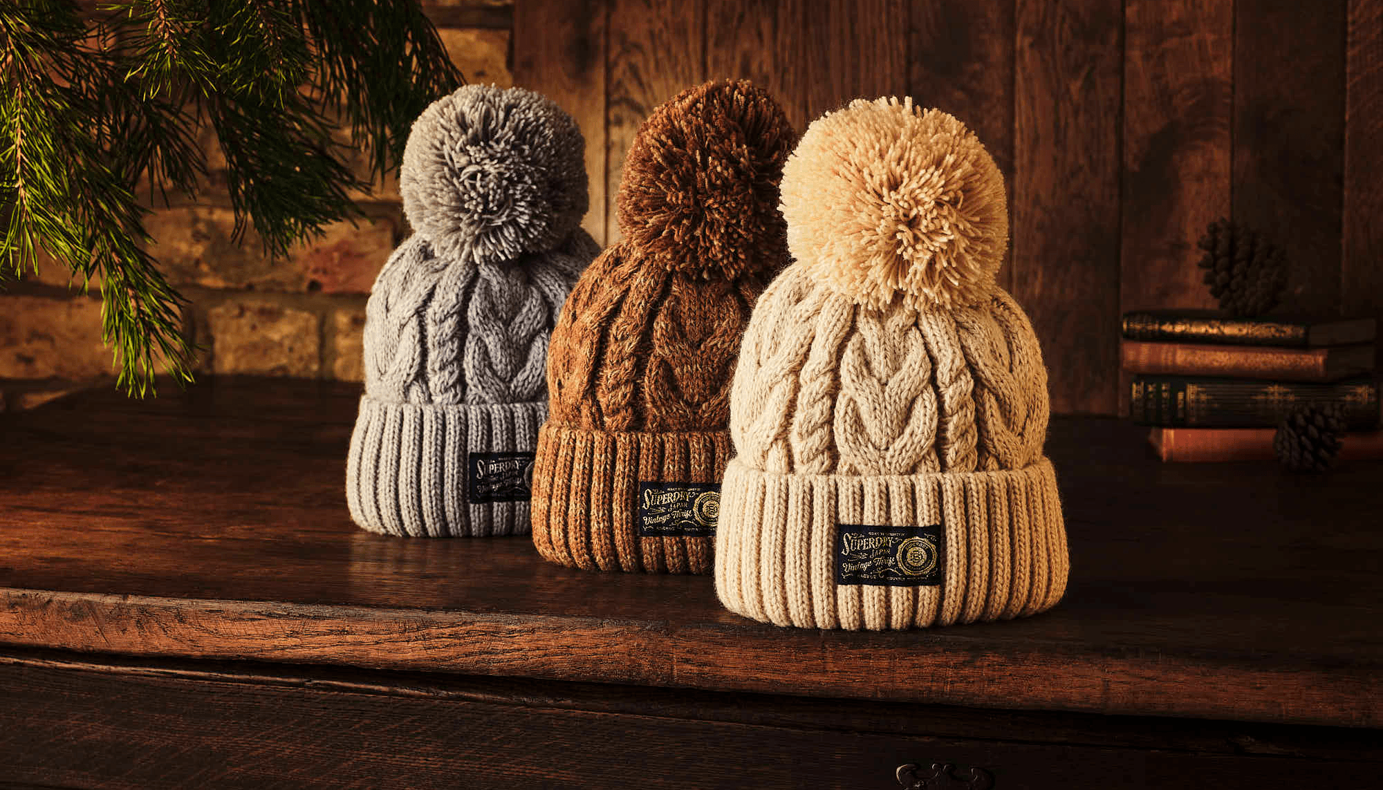 Cozy knit beanies with pom-poms in gray, brown, and beige on a wooden table.