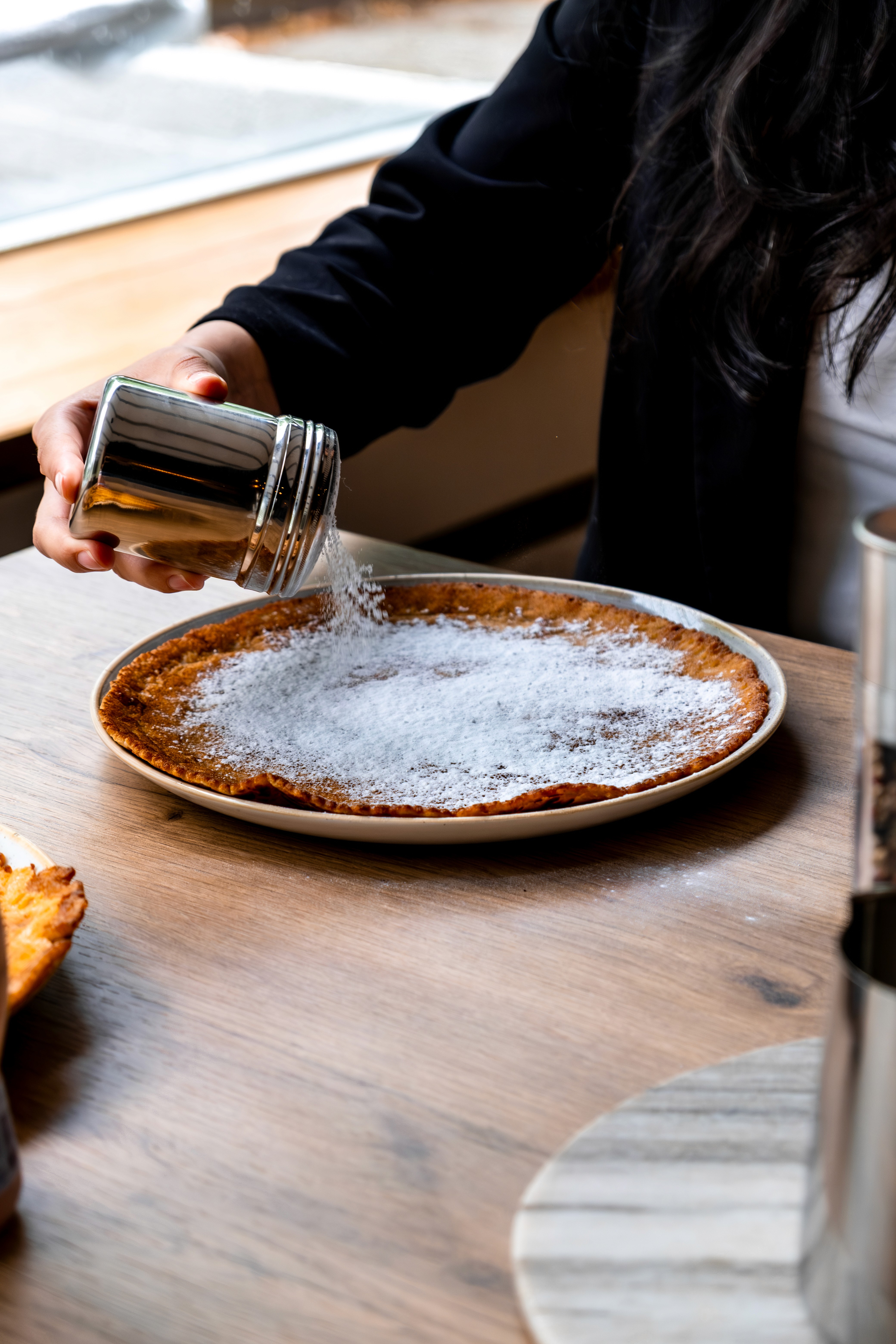 Poedersuiker wordt vers over een pannenkoek gestrooid bij Pan & Cook.