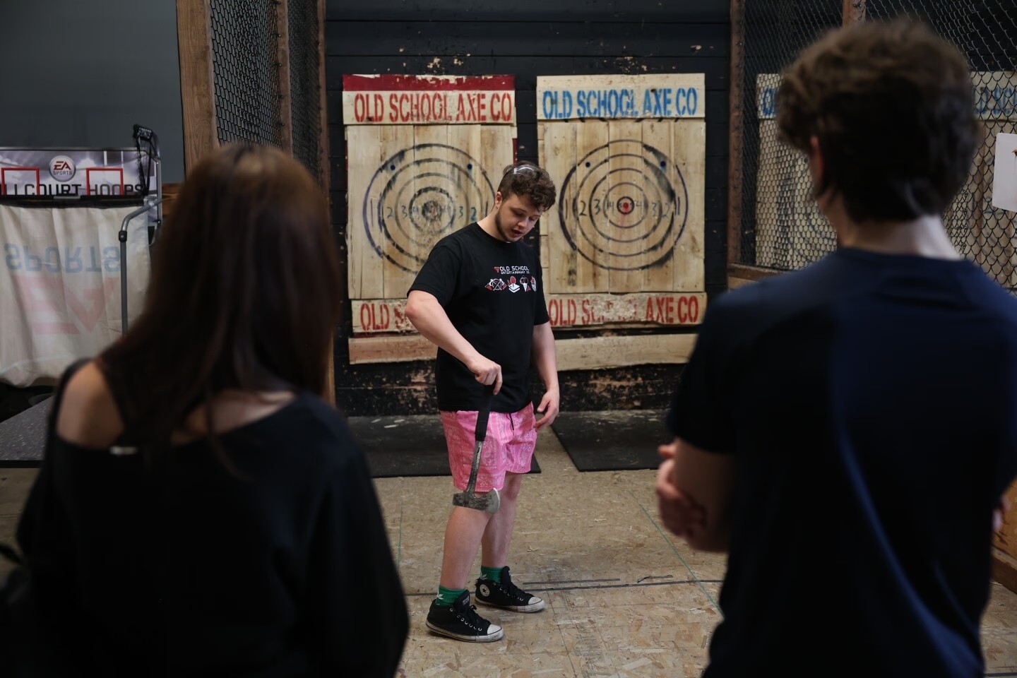 A man prepares to throw an axe at a target, watched by two other people. Axe throwing at Old School Axe Co.