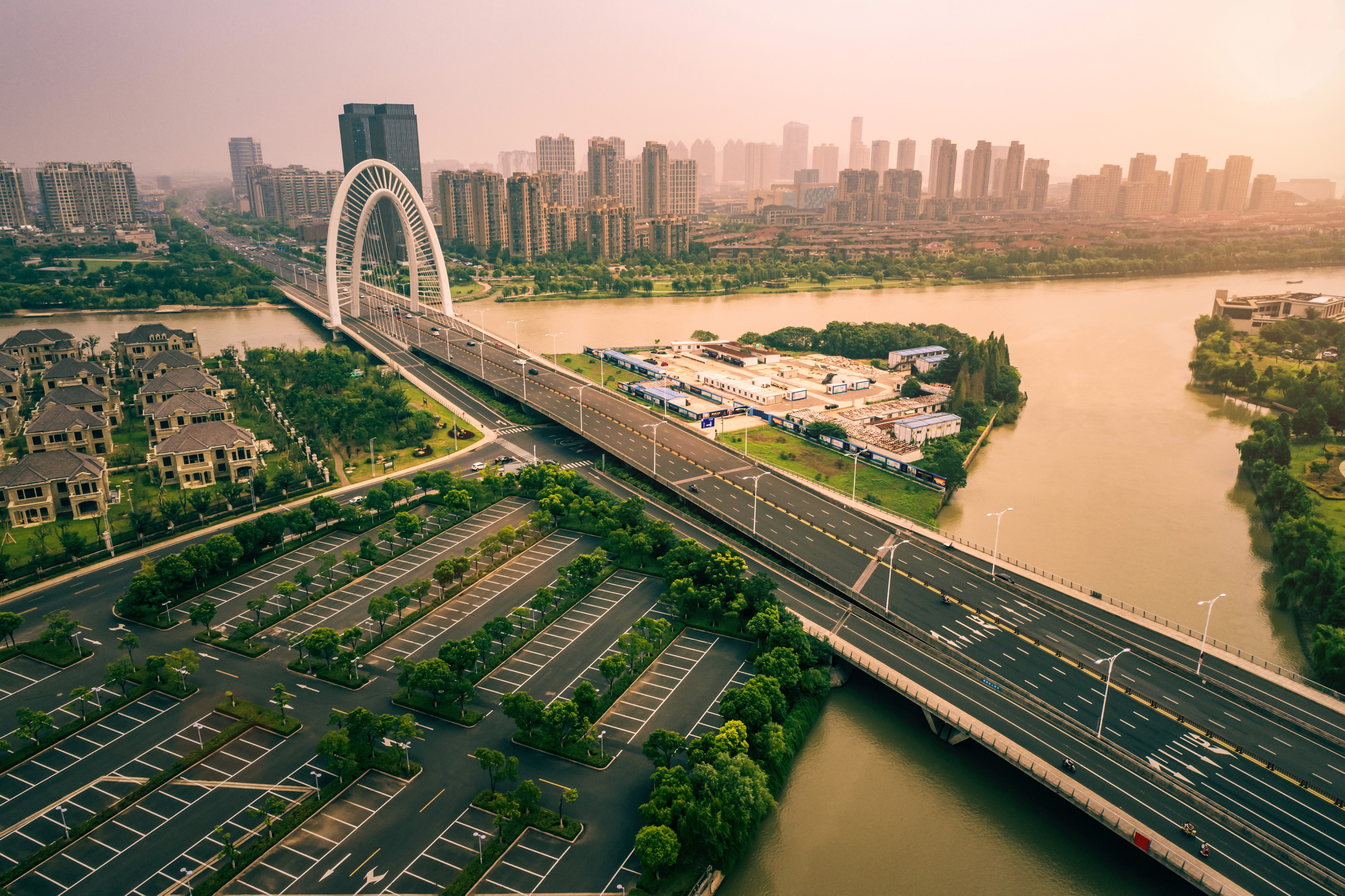 A rustic outdoor market stall displays an array of fresh produce including vibrant tomatoes, leafy greens, and a variety of olives, set against the backdrop of a picturesque rural Italian village.
