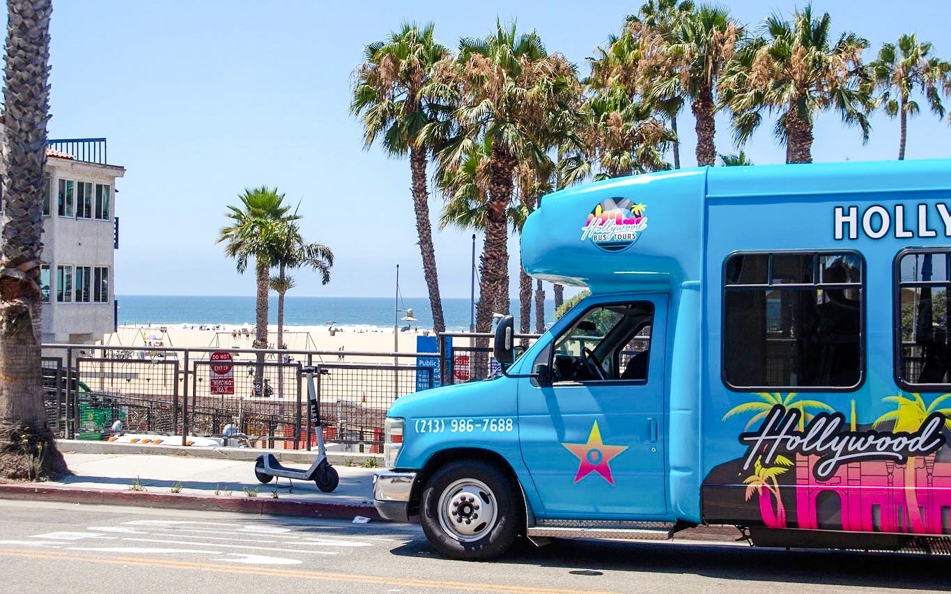 Hollywood bustochtvoertuig nabij het strand van Los Angeles met palmbomen.