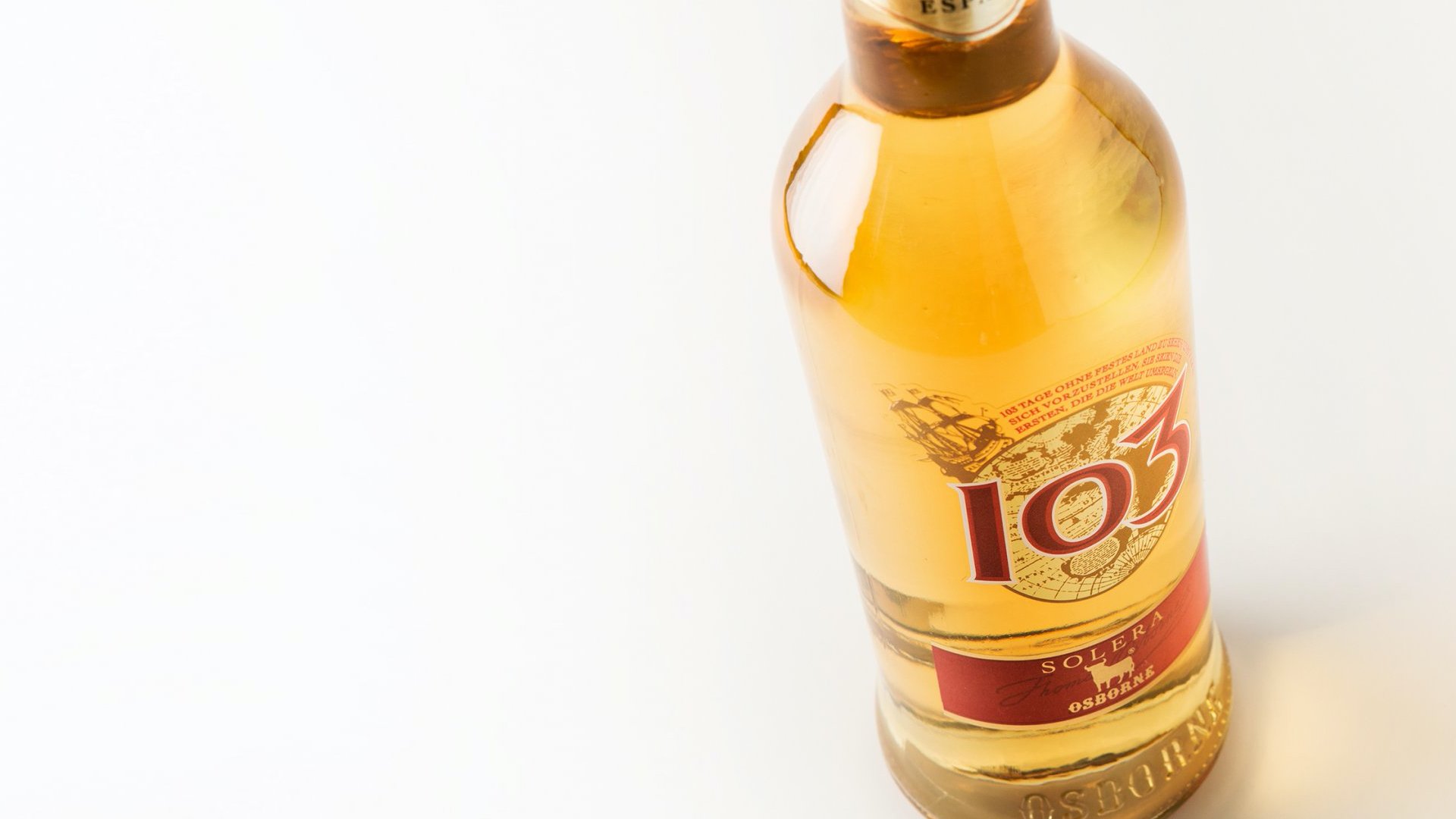 A bottle of golden-colored liquor labeled "103" stands upright on a plain white background. The label features a ship, suggesting a nautical theme.
