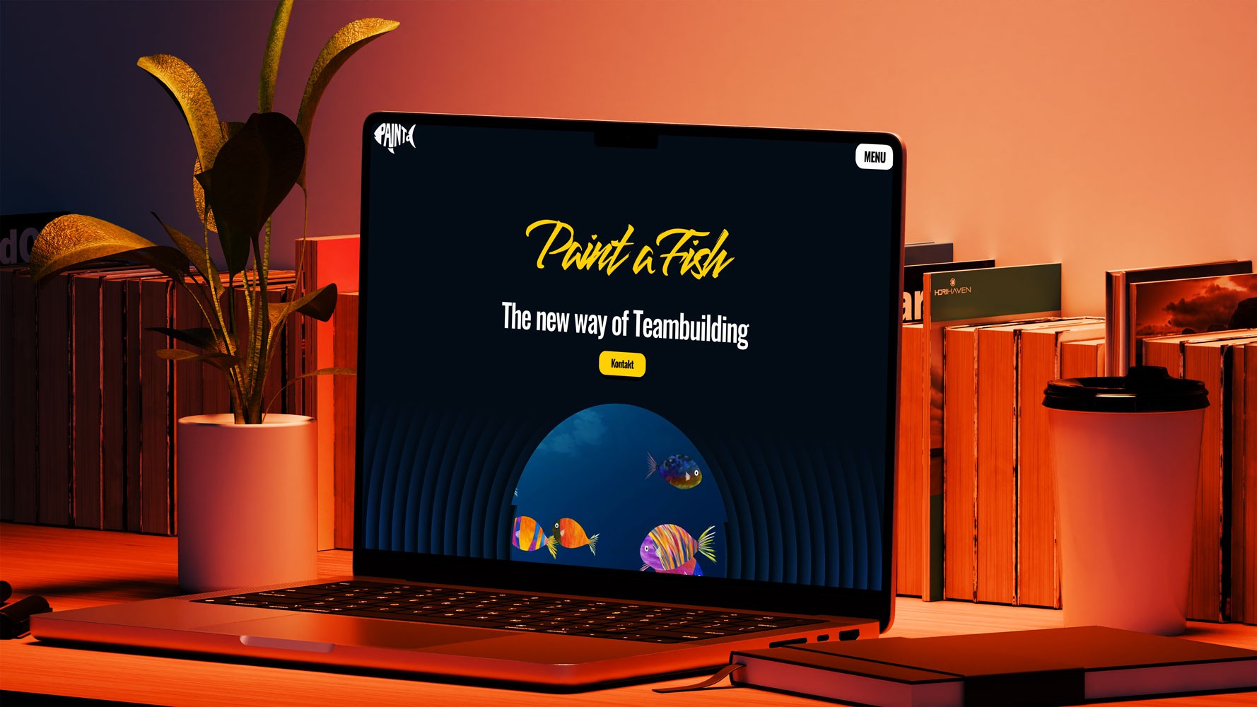 Mockup eines Laptops auf einem Schreibtisch mit der geöffneten Website ‚Paint a Fish‘. Auf dem Bildschirm ist das Logo, der Claim ‚The new way of Teambuilding‘ und farbenfrohe Fische als Designelemente sichtbar.