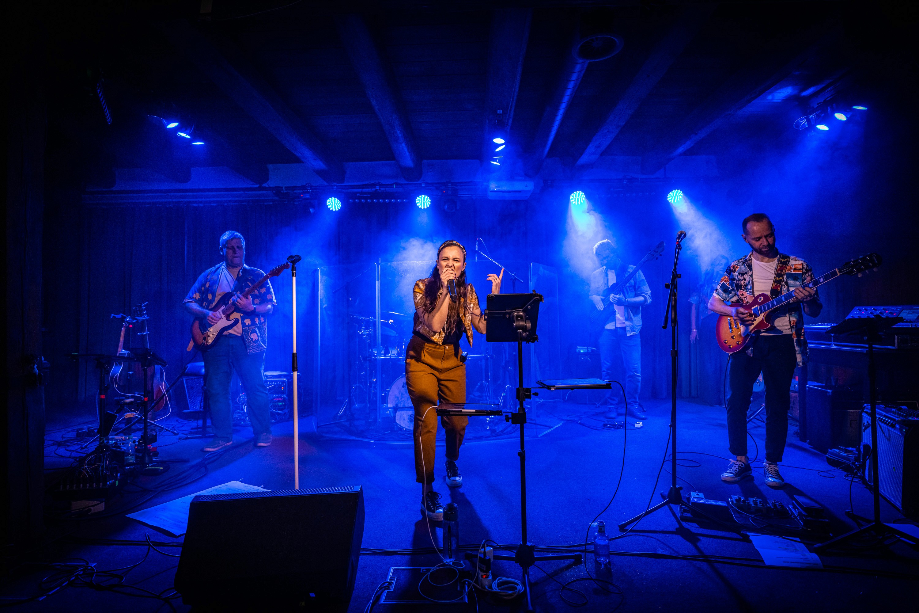 Live concert performance photographed on stage with musicians under blue stage lighting.