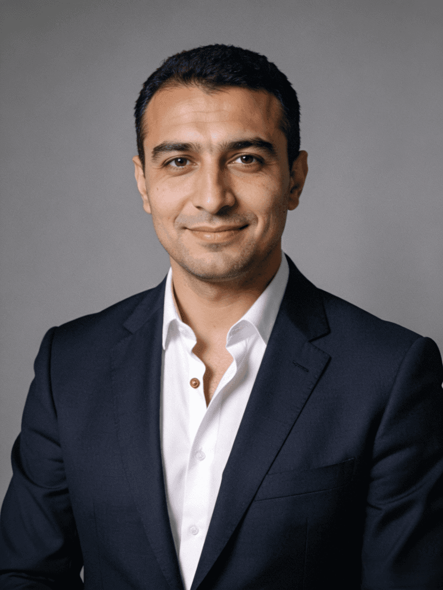 A man with dark curly hair and glasses smiling in a portrait.