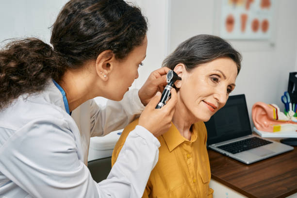 A healthcare professional examines a patient's ear with an otoscope in a medical office setting.