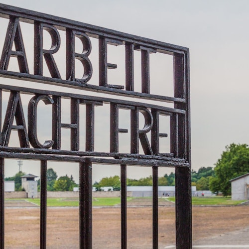 멀리 건물과 나무가 보이는 황량한 개방 지역을 내려다보고 있는 'Arbeit Macht Frei'라는 문구가 새겨진 주철 문.