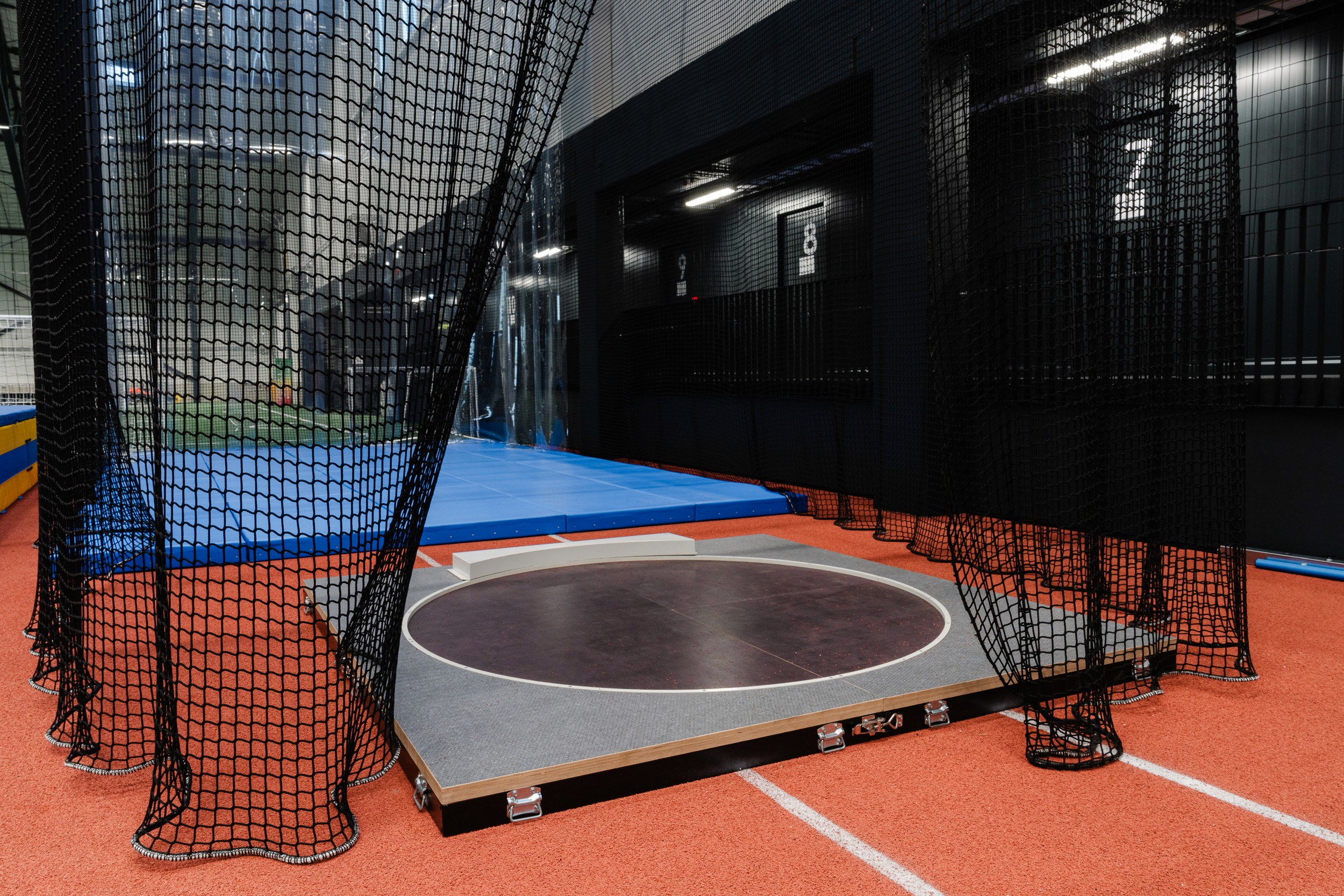 Close interior view of a shot-put or throwing practice area enclosed by netting, with numbered dark bays.