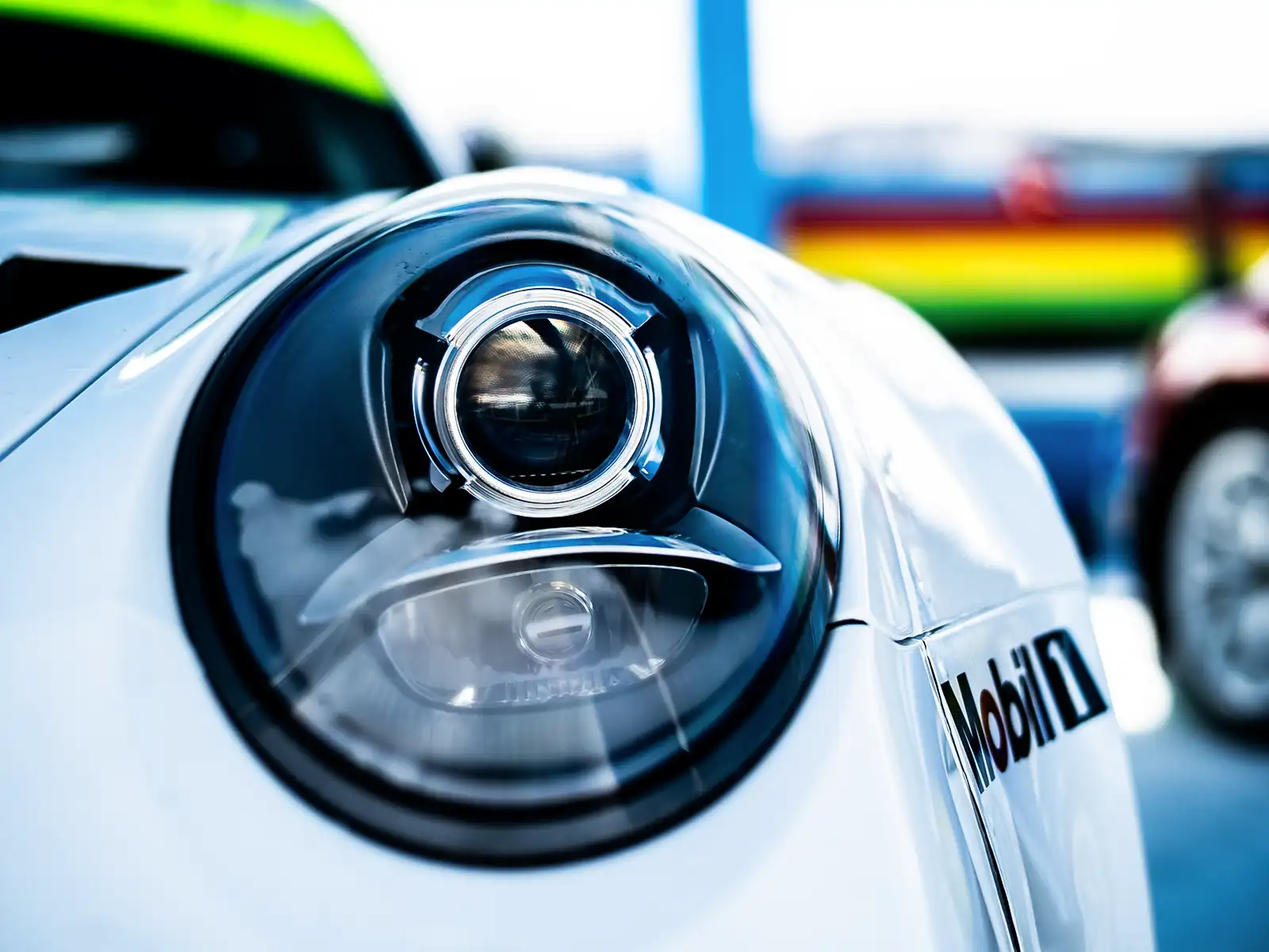 Close-up of a white Porsche headlight, showcasing its shiny exterior and design details.