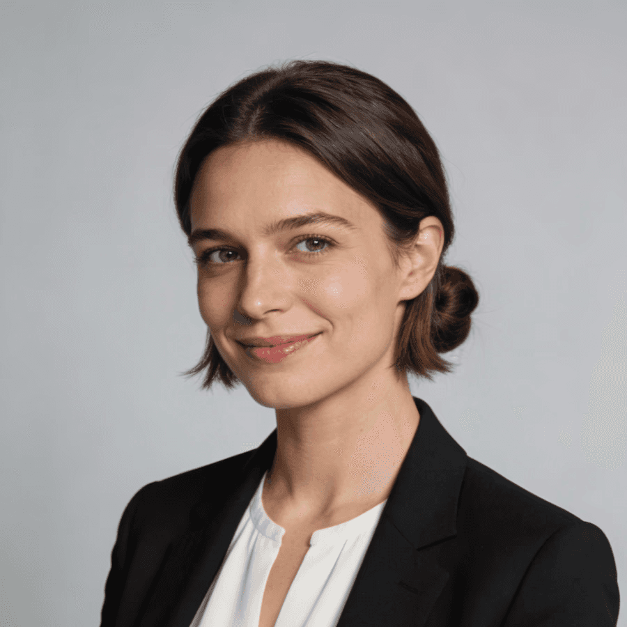 Professional portrait of a woman in a black blazer and white blouse, smiling warmly against a neutral gray background.