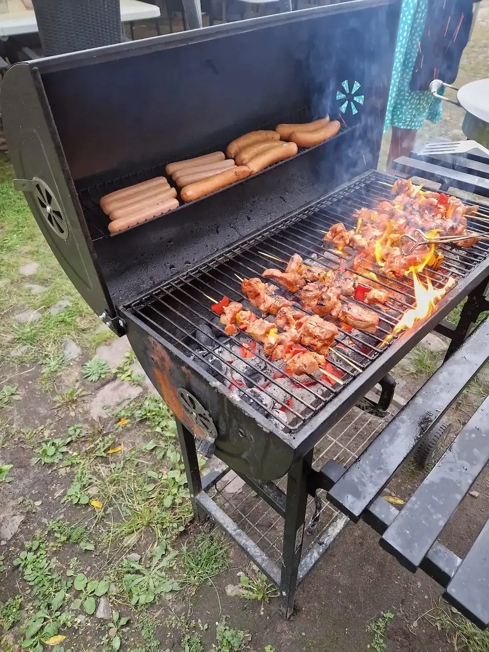 Korv och grillspett tillagas på grill utomhus under en gemensam aktivitet.