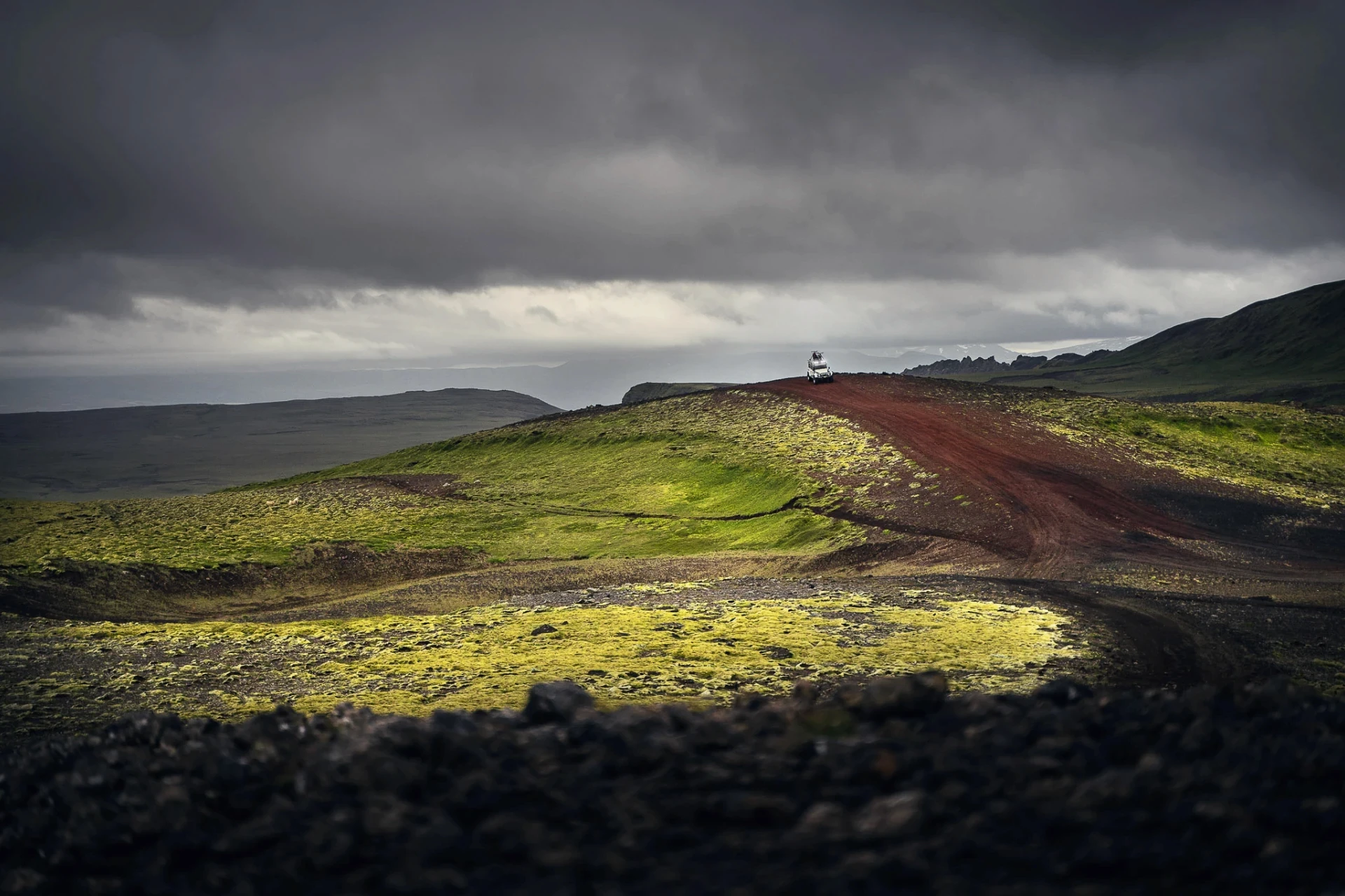 4x4 driving on a red dirt road across mossy hills under dark clouds.