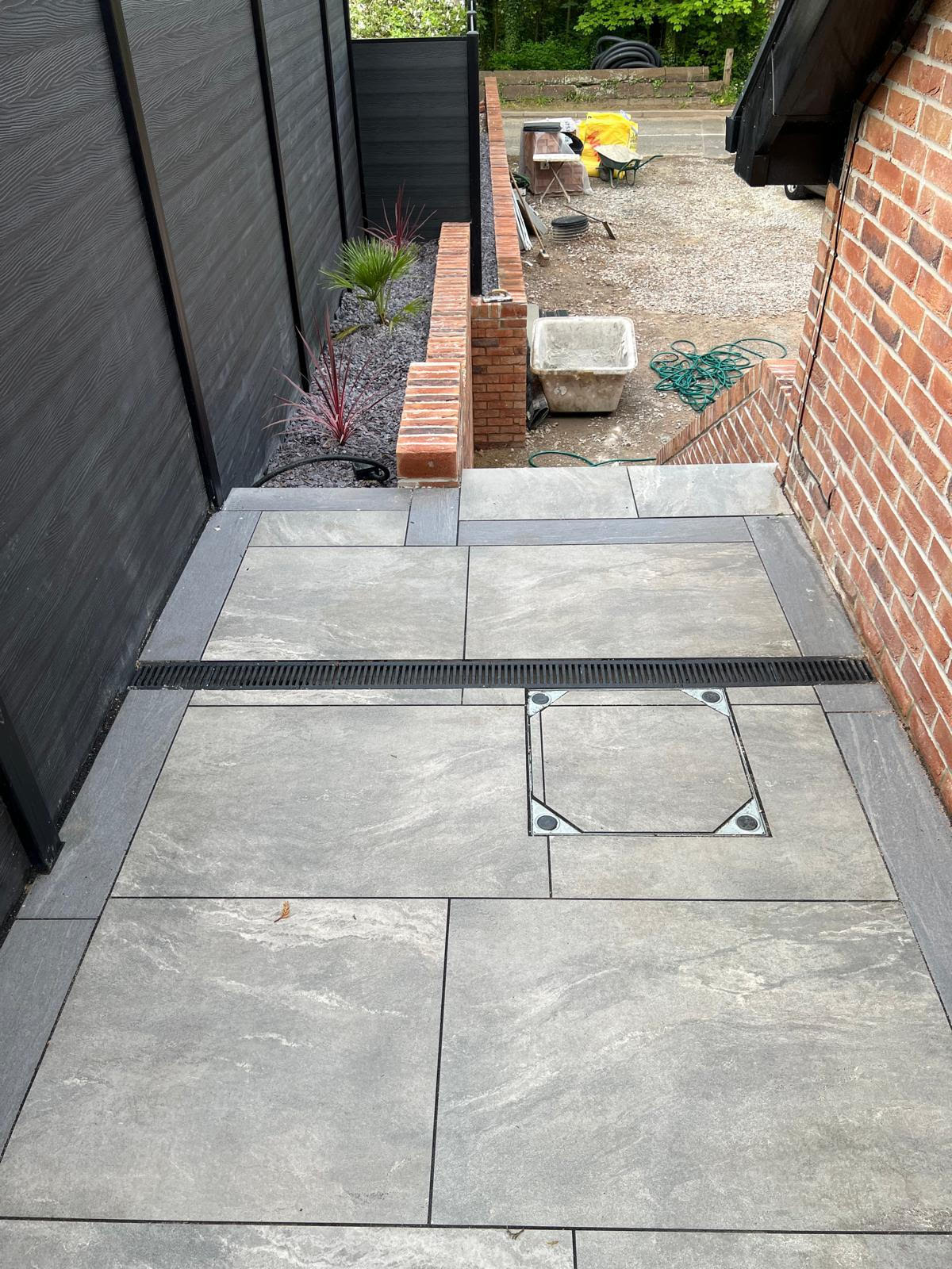 LK Landscaping and Groundworks project: Modern patio installation with grey porcelain tiles, brick edging, and contemporary planting. Showcasing drainage solutions and expert hardscaping in Cheshire garden transformation