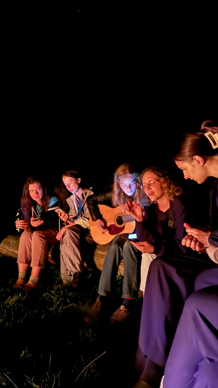 Junge Leute sitzen um ein Lagerfeuer herum, singen und spielen Gitarre.