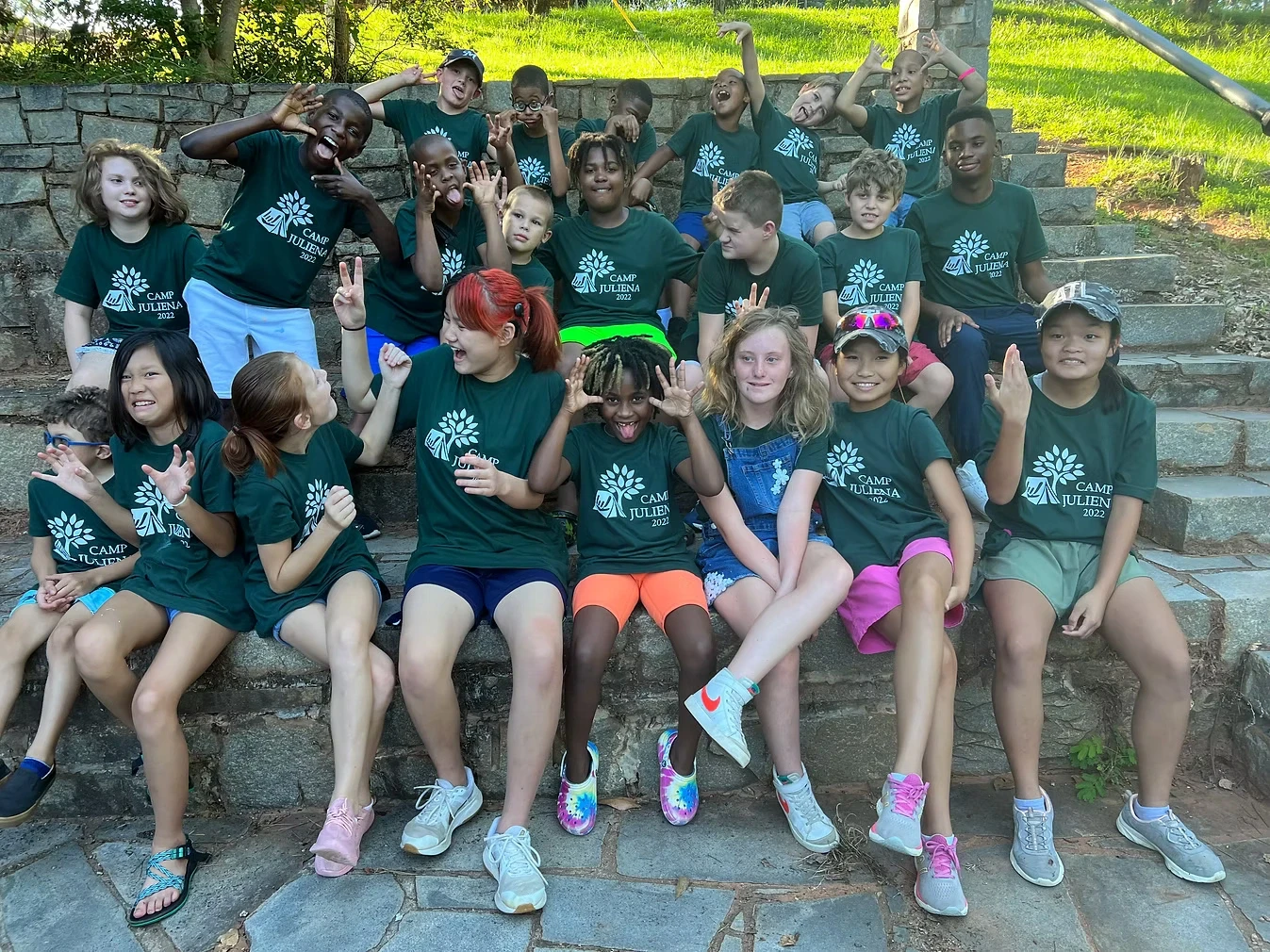 Group of campers in green Camp Juliena shirts making silly faces and poses outdoors.