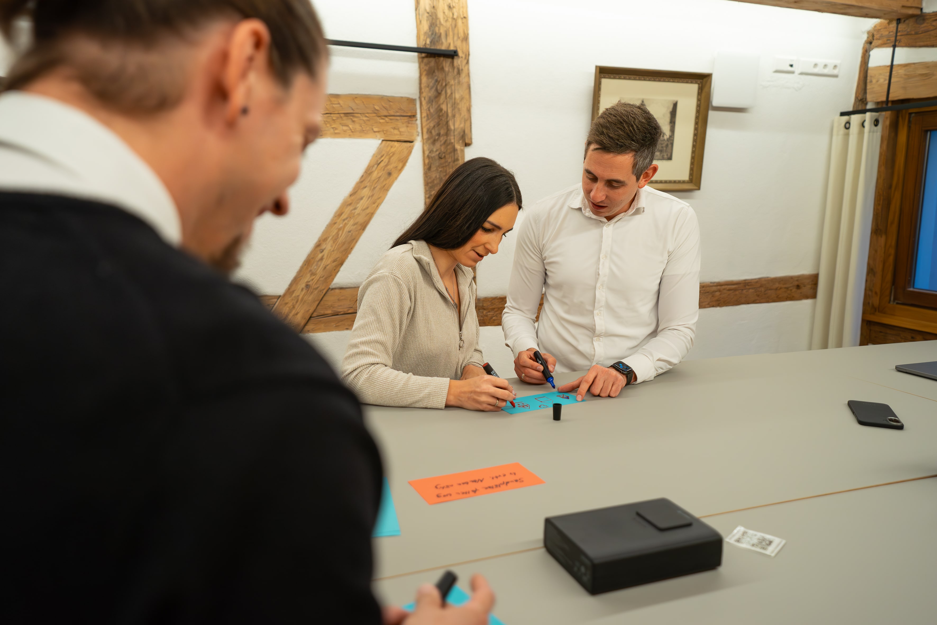 Drei Personen diskutieren an einem Tisch, prüfen Dokumente und tauschen Ideen in einer kollaborativen Umgebung aus.