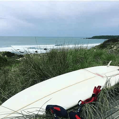 Beach scene with surfboard on grassy dune – surfboard rental in Melbourne