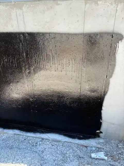 Rub-R-Proof black ashphalt waterproof coating reflecting sunlight on a concrete foundation