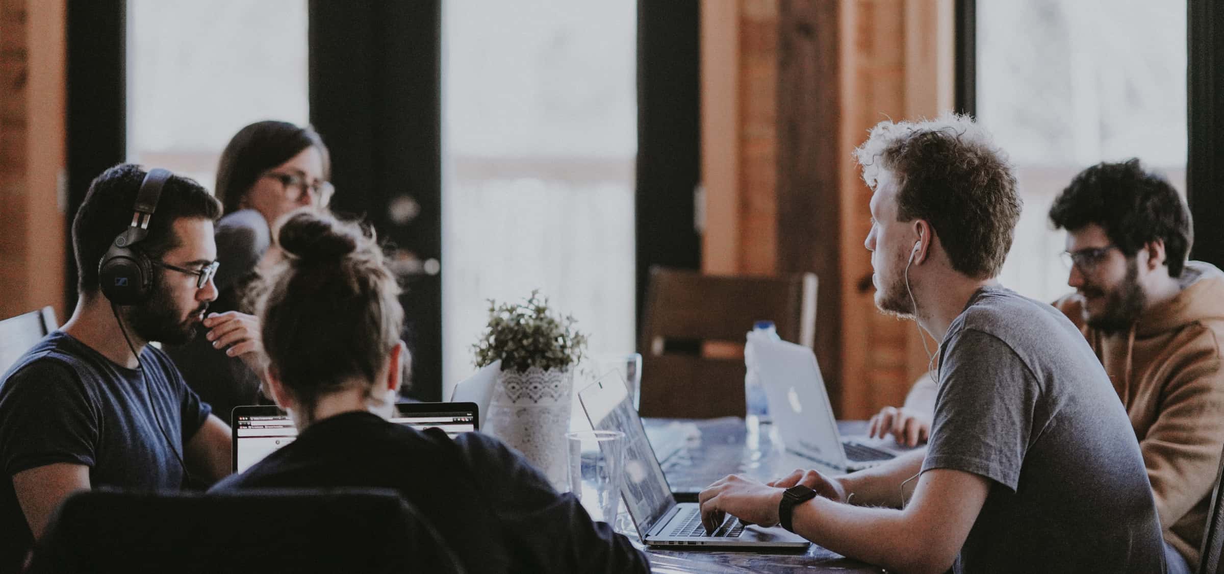 A group of IT support employees sitting at a large table and working on their laptops.