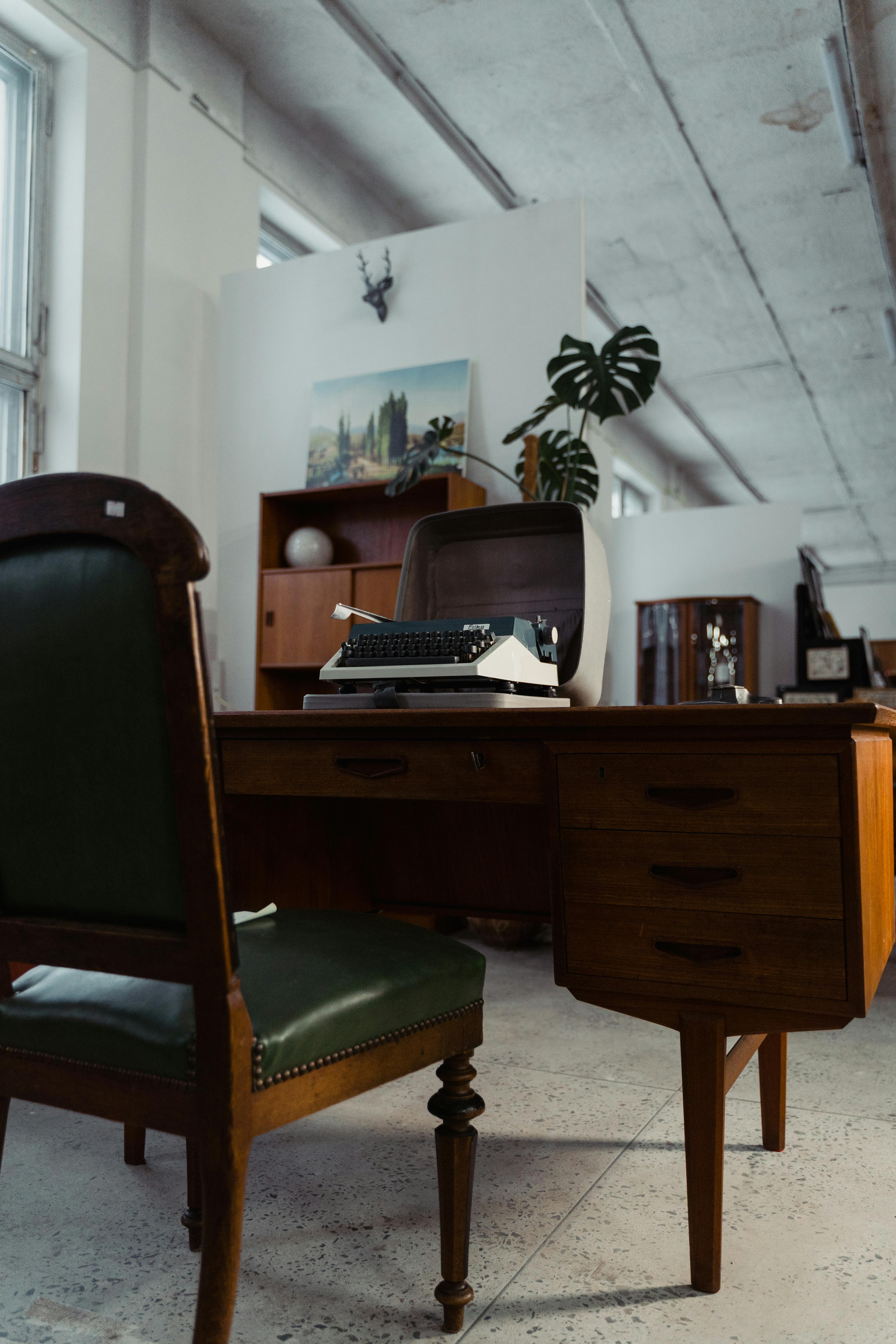 Vintage office with a typewriter, wooden desk, and green leather chair.