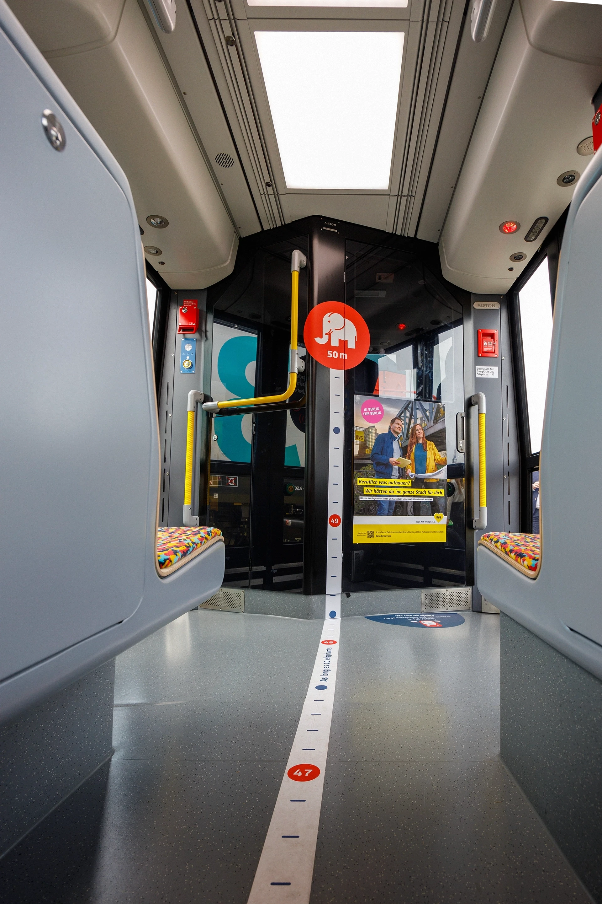  „Alstom Flexity Straßenbahn Innenraum: Blick durch den Fahrgastraum mit farbigen Sitzen, 50-Meter-Längenmarkierung und Elefanten-Grafik