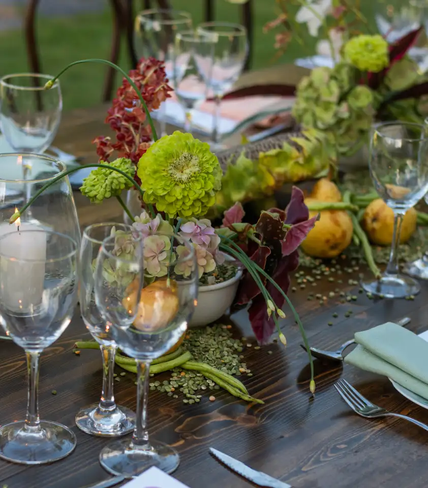 Mesa al aire libre con flores verdes y lilas, diseño floral estacional con frutas y semillas naturales.