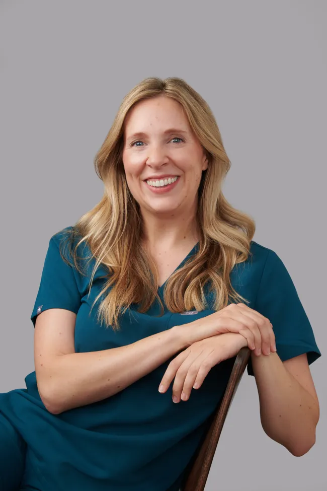 Trish Mueller, founder of Lift and Revive, smiling in teal medical scrubs against a neutral background