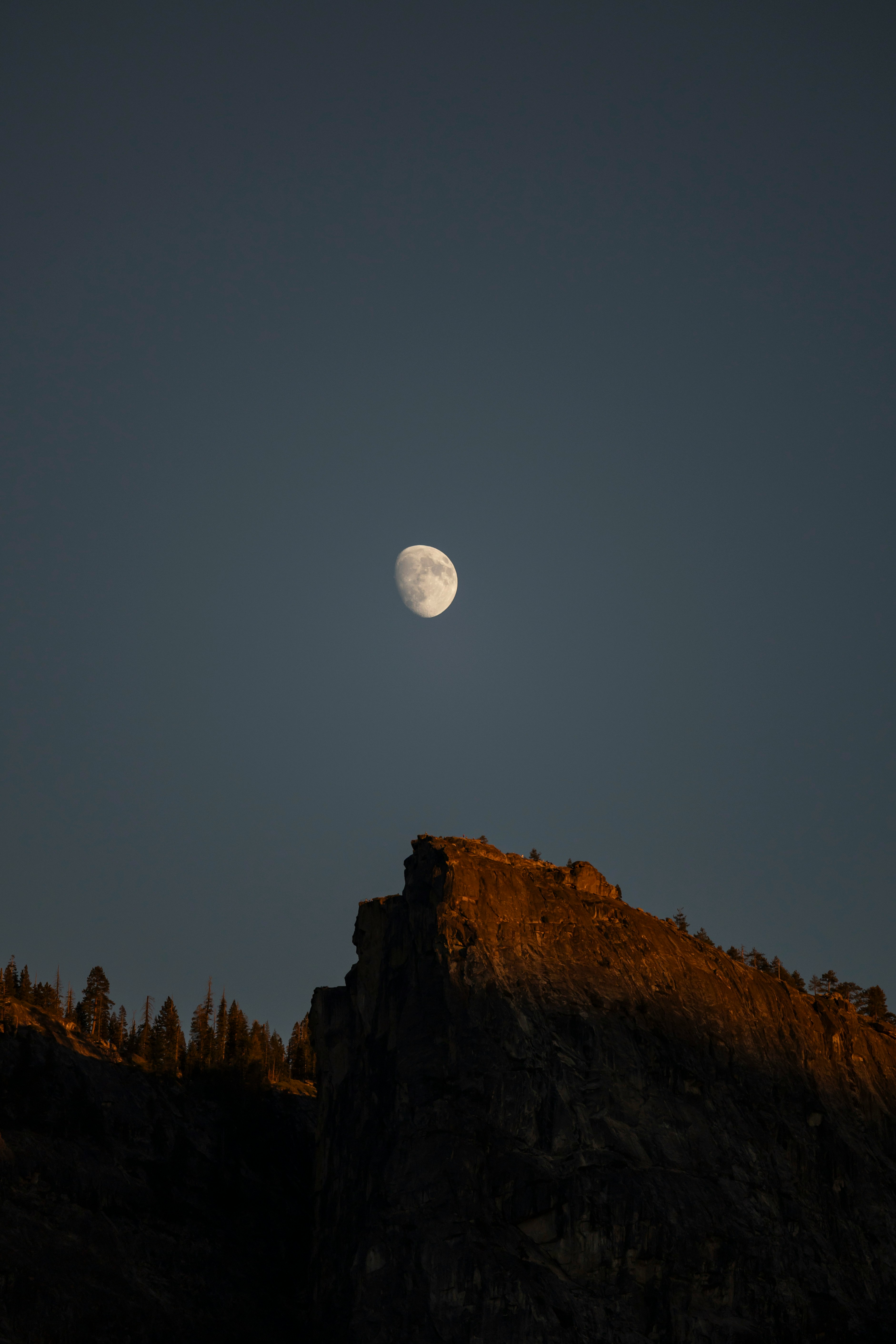 The moon hangs above a sunlit mountain peak.