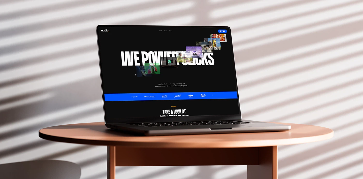 A laptop on a round table displaying a dark-themed marketing website with the headline “We Power Clicks.”