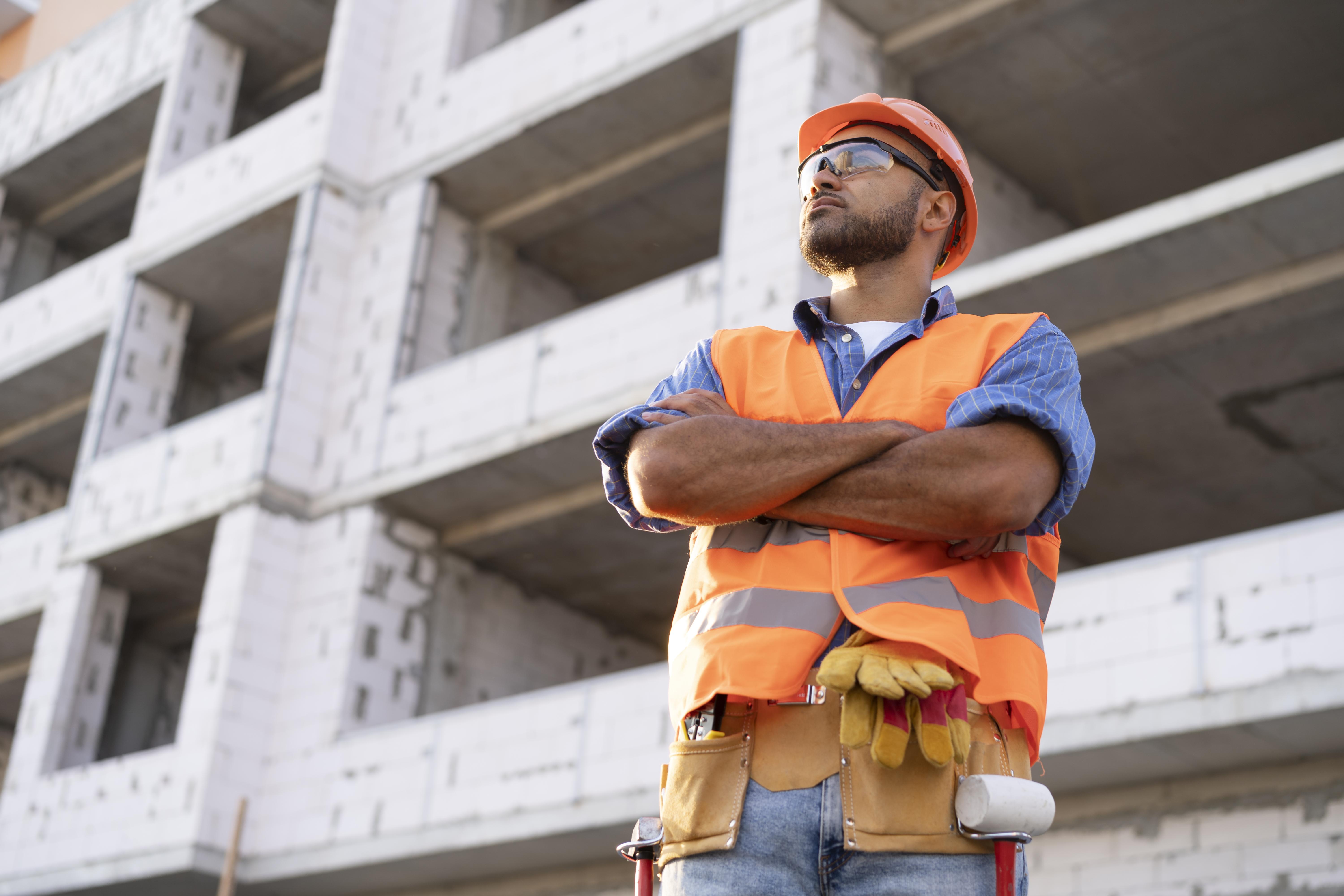 Trabalhador em uma obra de construção civil, utilizando EPIs, de braços cruzados