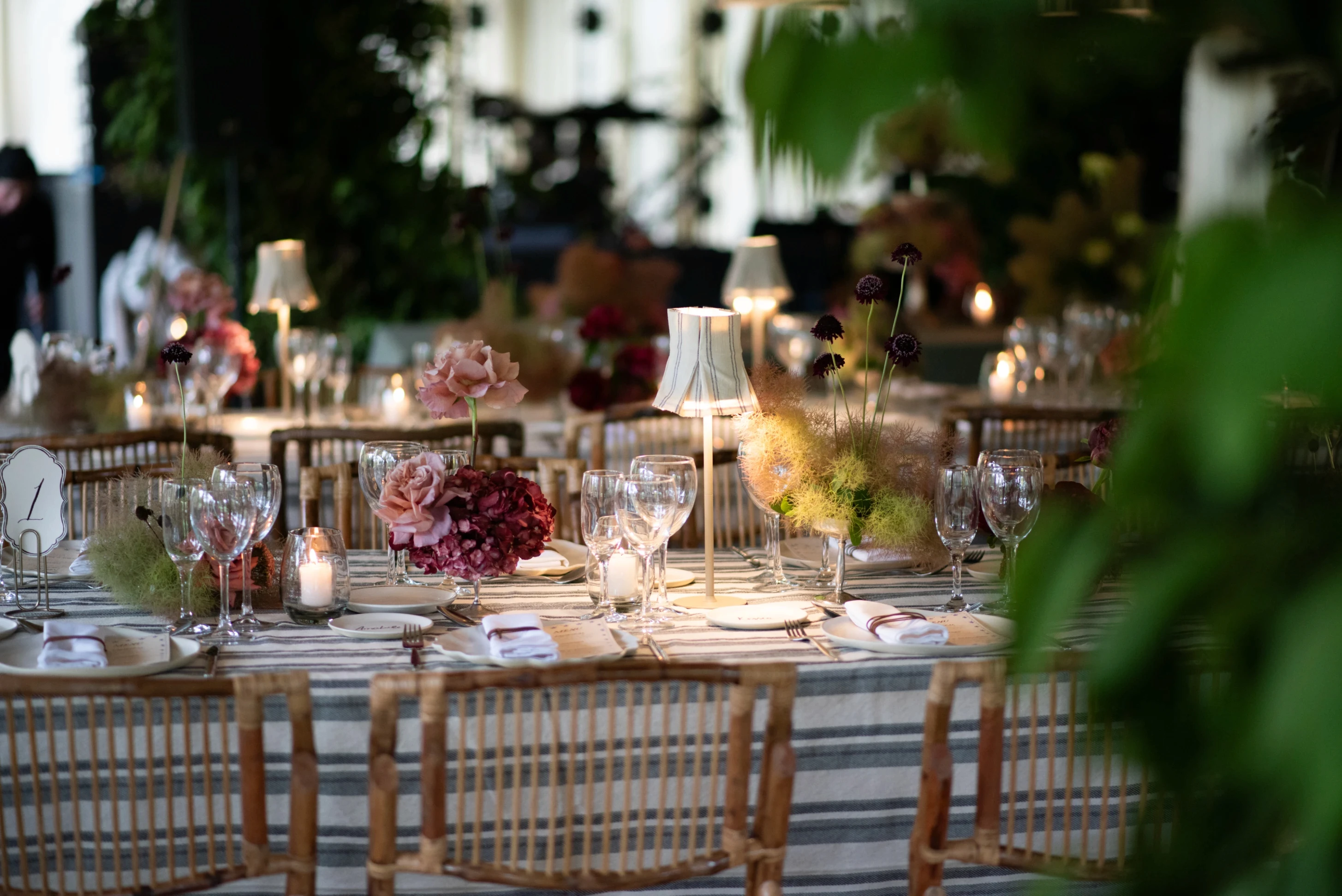 Detalle de una mesa de recepción de boda con manteles a rayas, sillas de caña y centros de mesa florales.