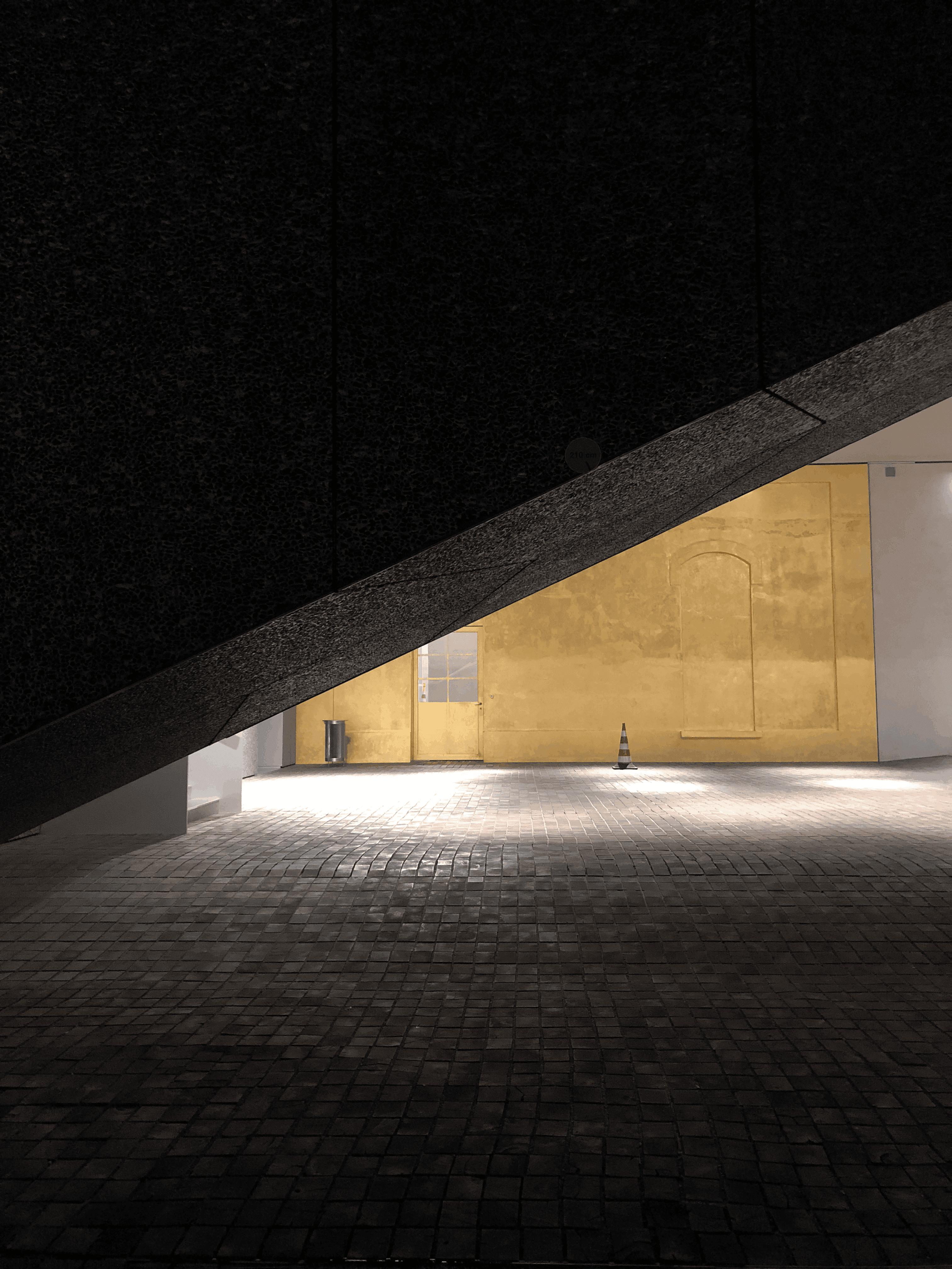 Minimalist architectural space with a dramatic diagonal ceiling and golden wall