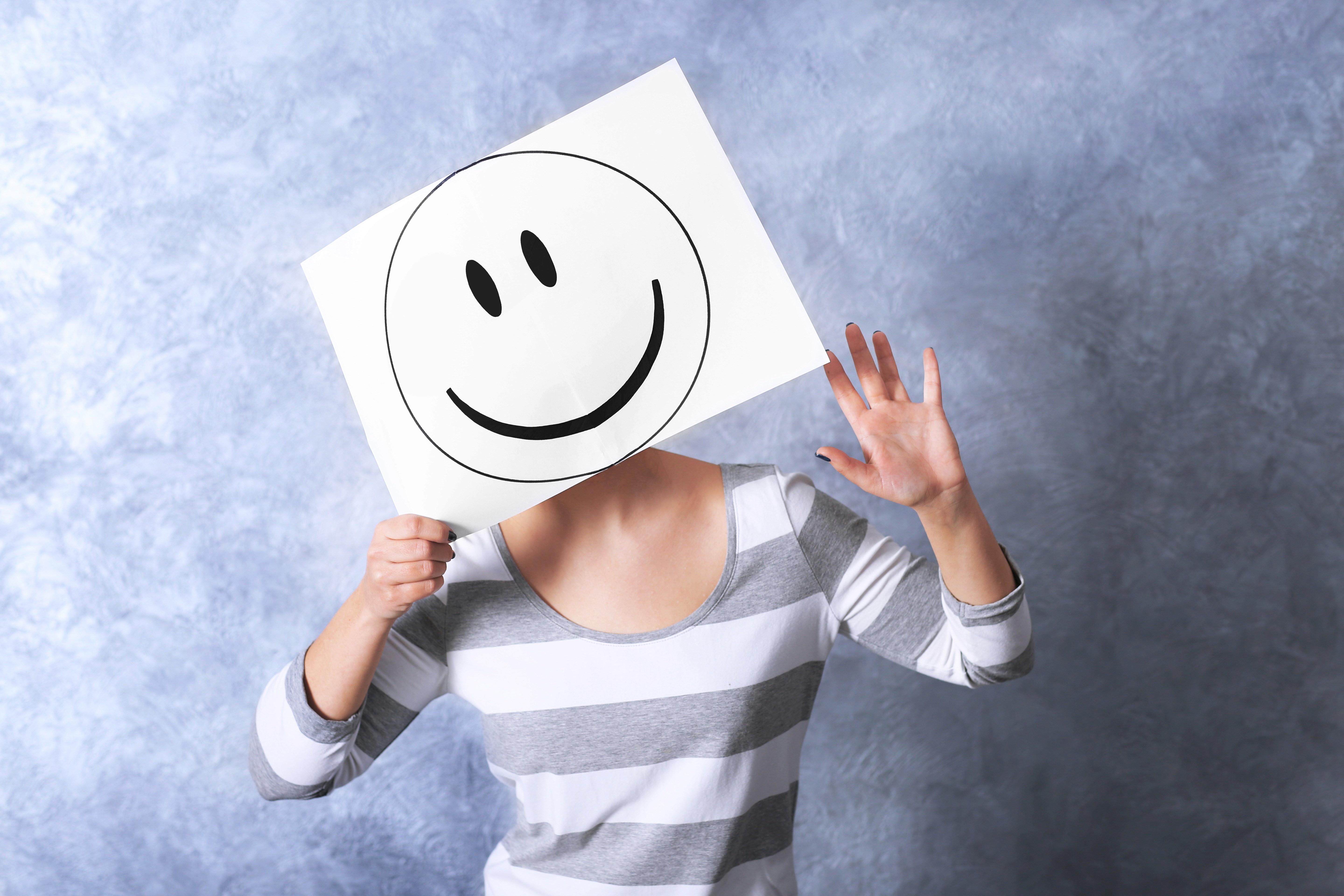 Woman holding a paper drawn smiley in front of her face