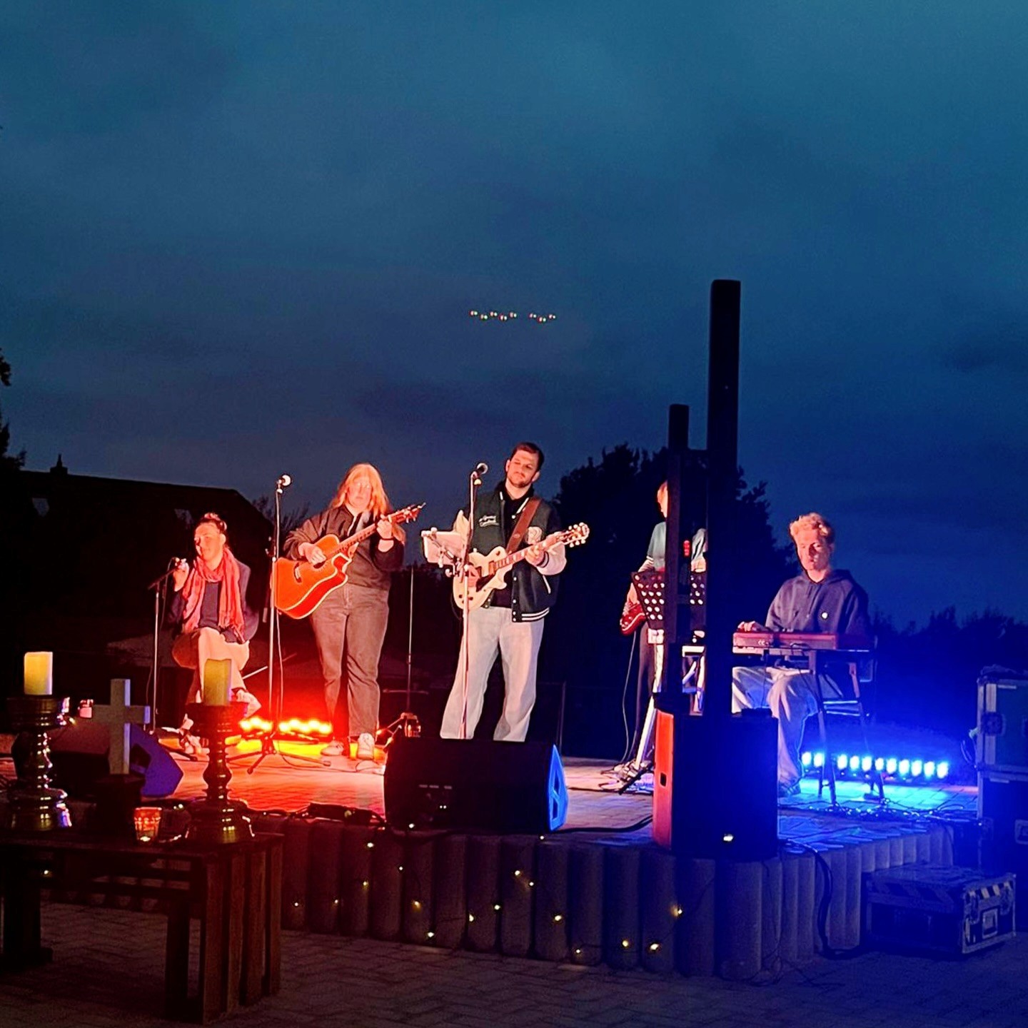 Eine Band steht nachts auf einer beleuchteten Außenbühne; die Szene ist in blaues Bühnenlicht getaucht.