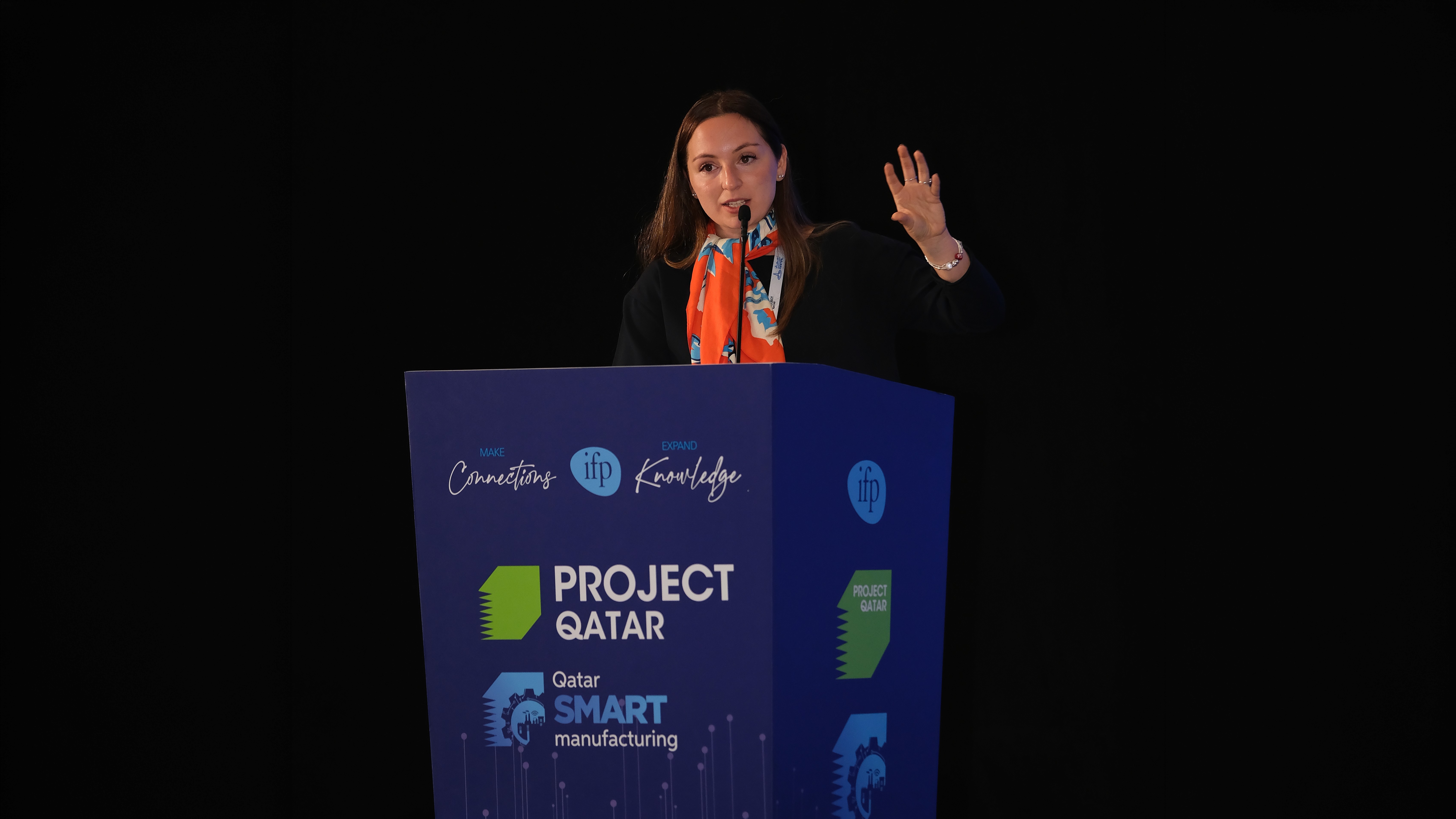 A woman speaks at a podium labeled "Project Qatar, Qatar Smart Manufacturing."