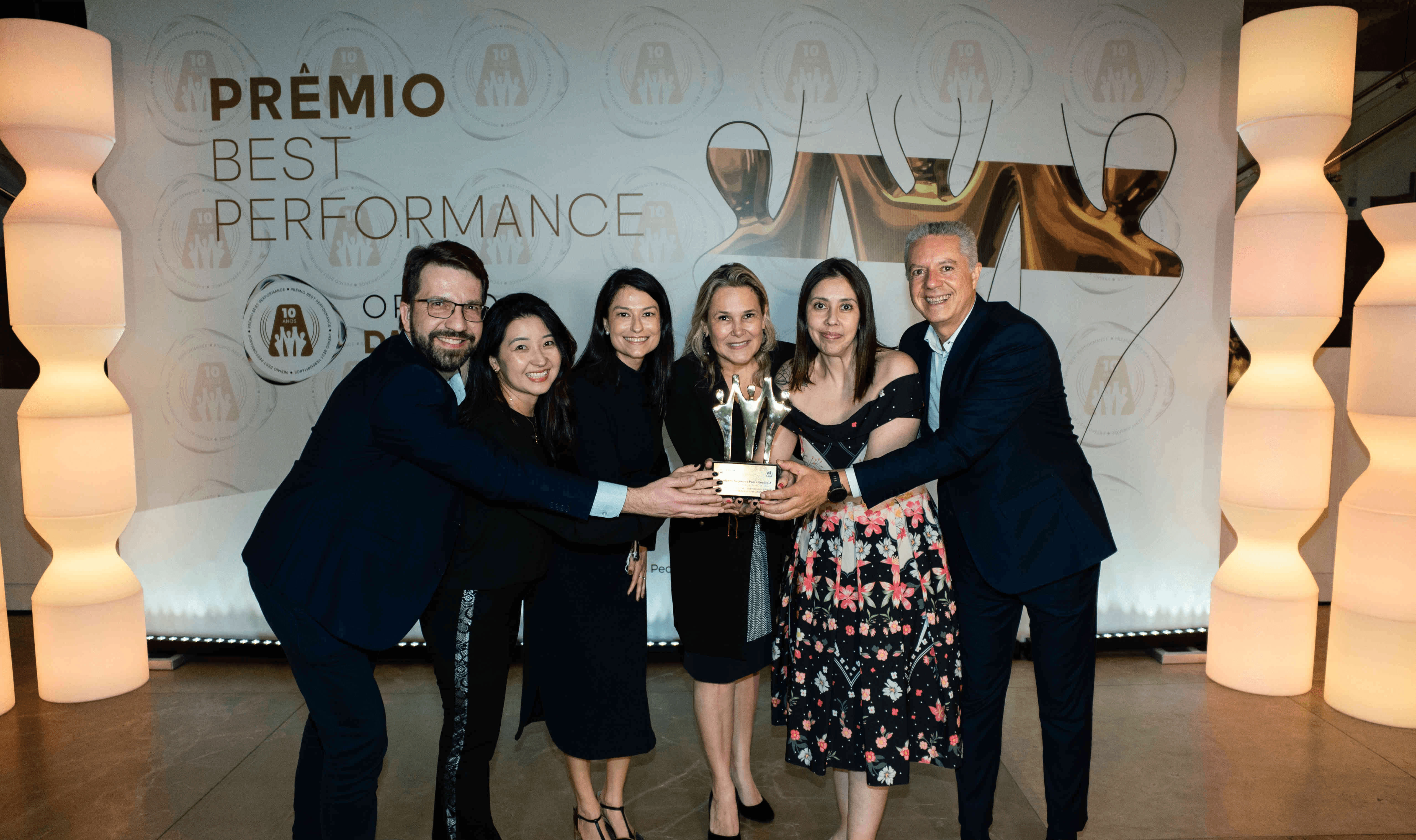 Executivos da Brasilprev Seguros posando com troféu ouro e certificado no palco do Prêmio Best Performance 2025