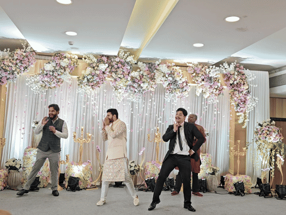Friends perform a coordinated dance on a flower-filled wedding stage