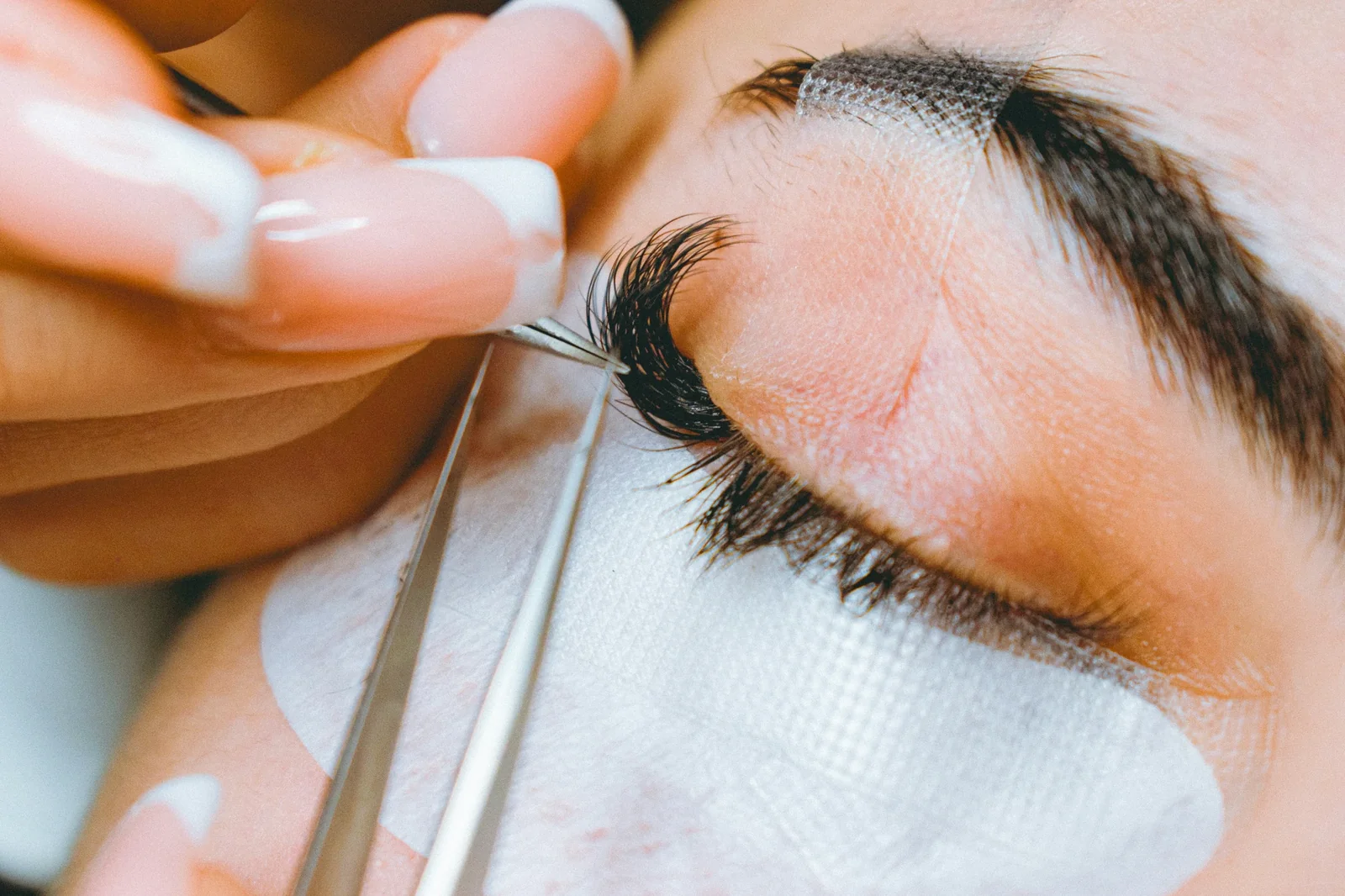 Close-up of a lash technician applying false eyelashes to a client's eye using tweezers.