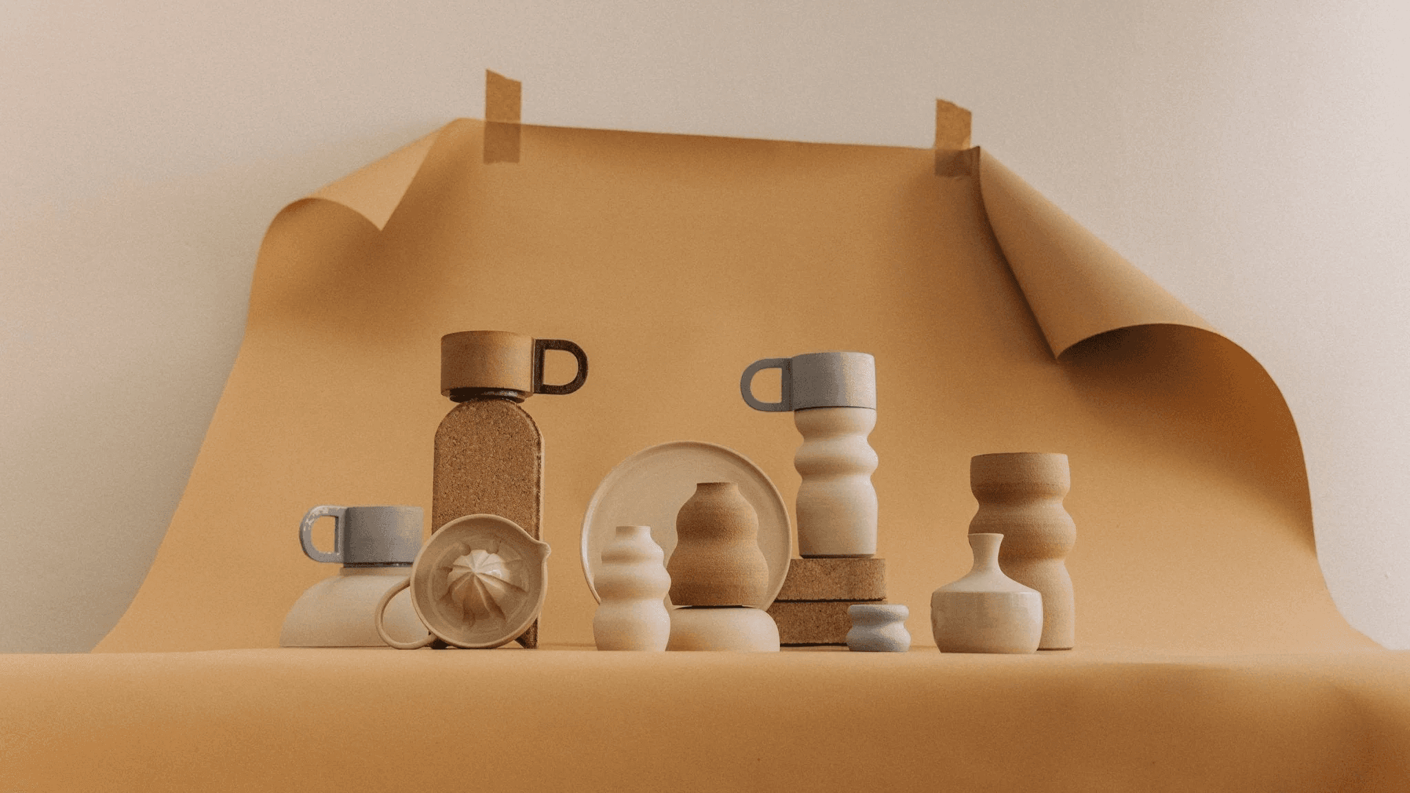 A minimalist arrangement of wooden and ceramic containers, including a juicer and various jars, is artistically displayed on a beige textured backdrop, creating an aesthetically pleasing and serene atmosphere.
