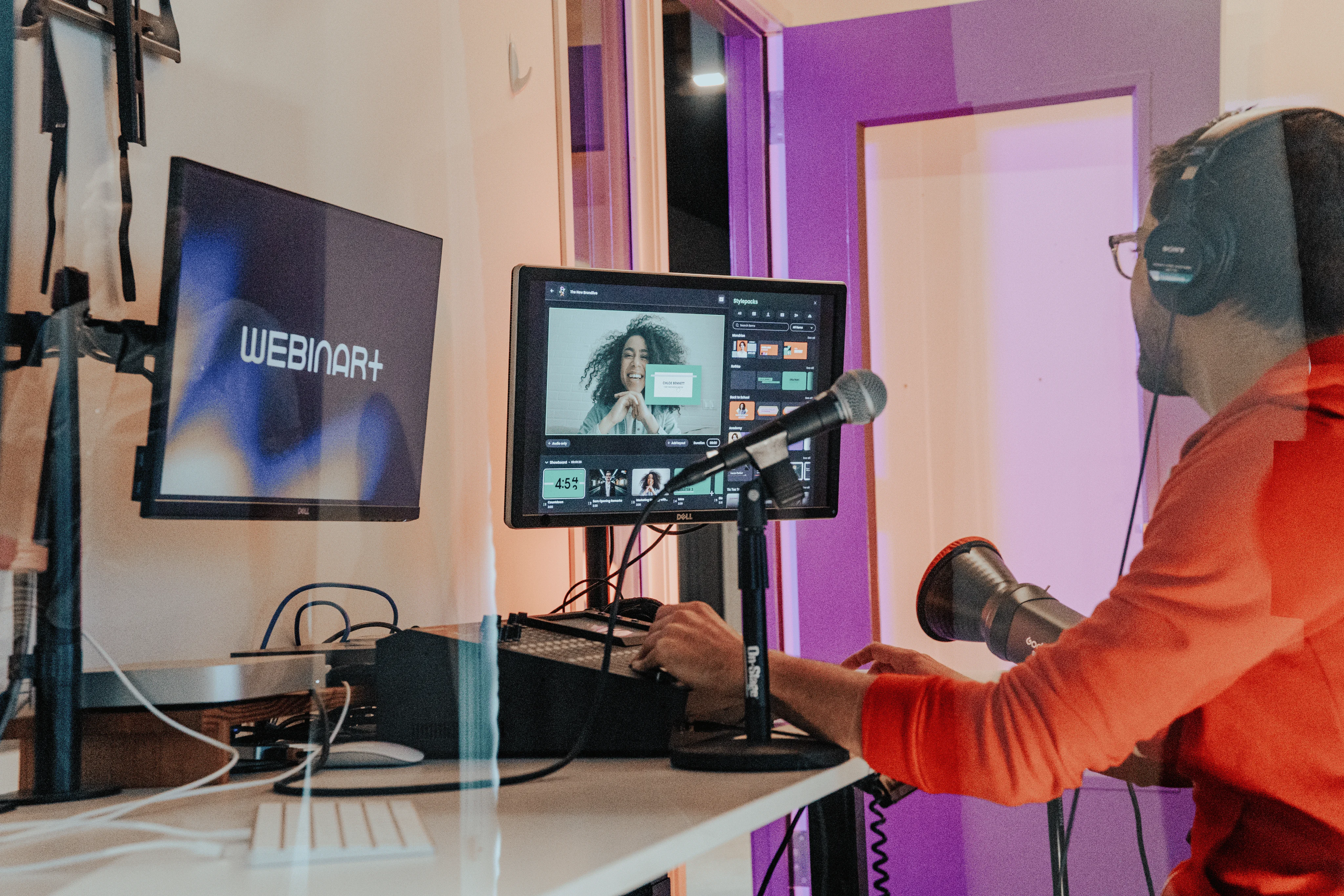 Brandlive producer in a red hoodie and headphones operating a live broadcast from a multi-screen production desk