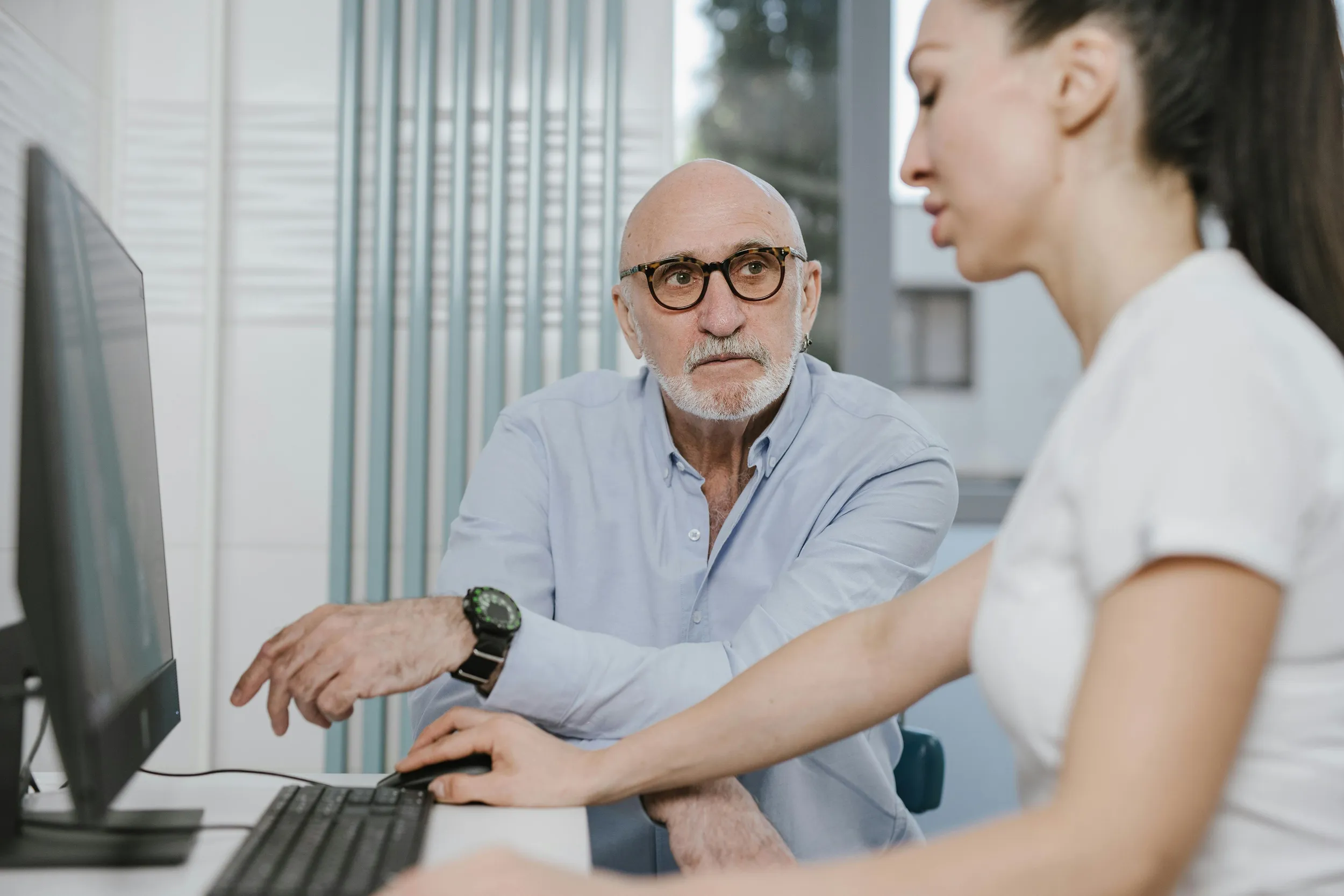 Senior doctor discussing patient data with colleague at computer in clinical office