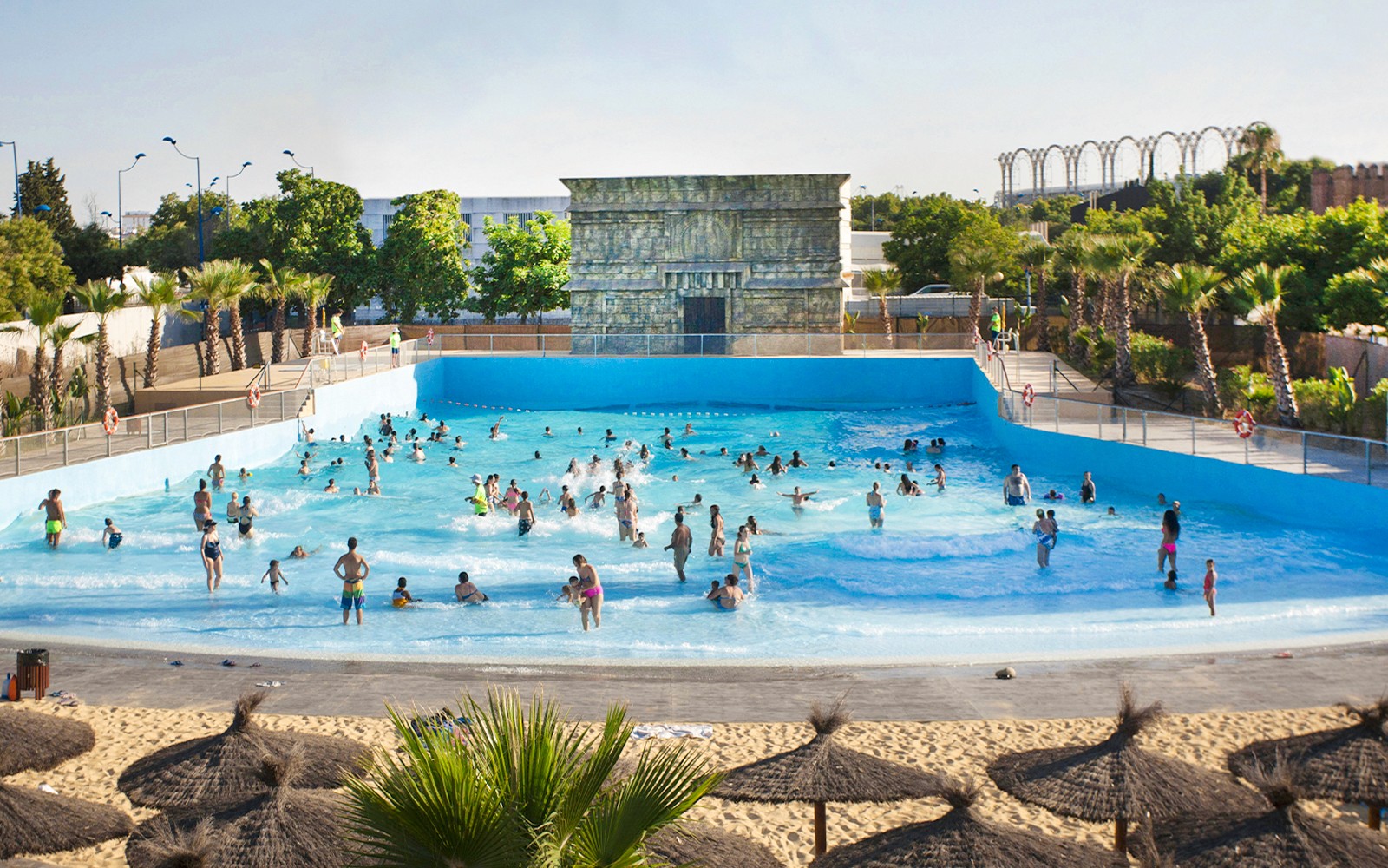 Visitors enjoying the wave pool at Isla Mágica, surrounded by palm trees and a sandy beach.