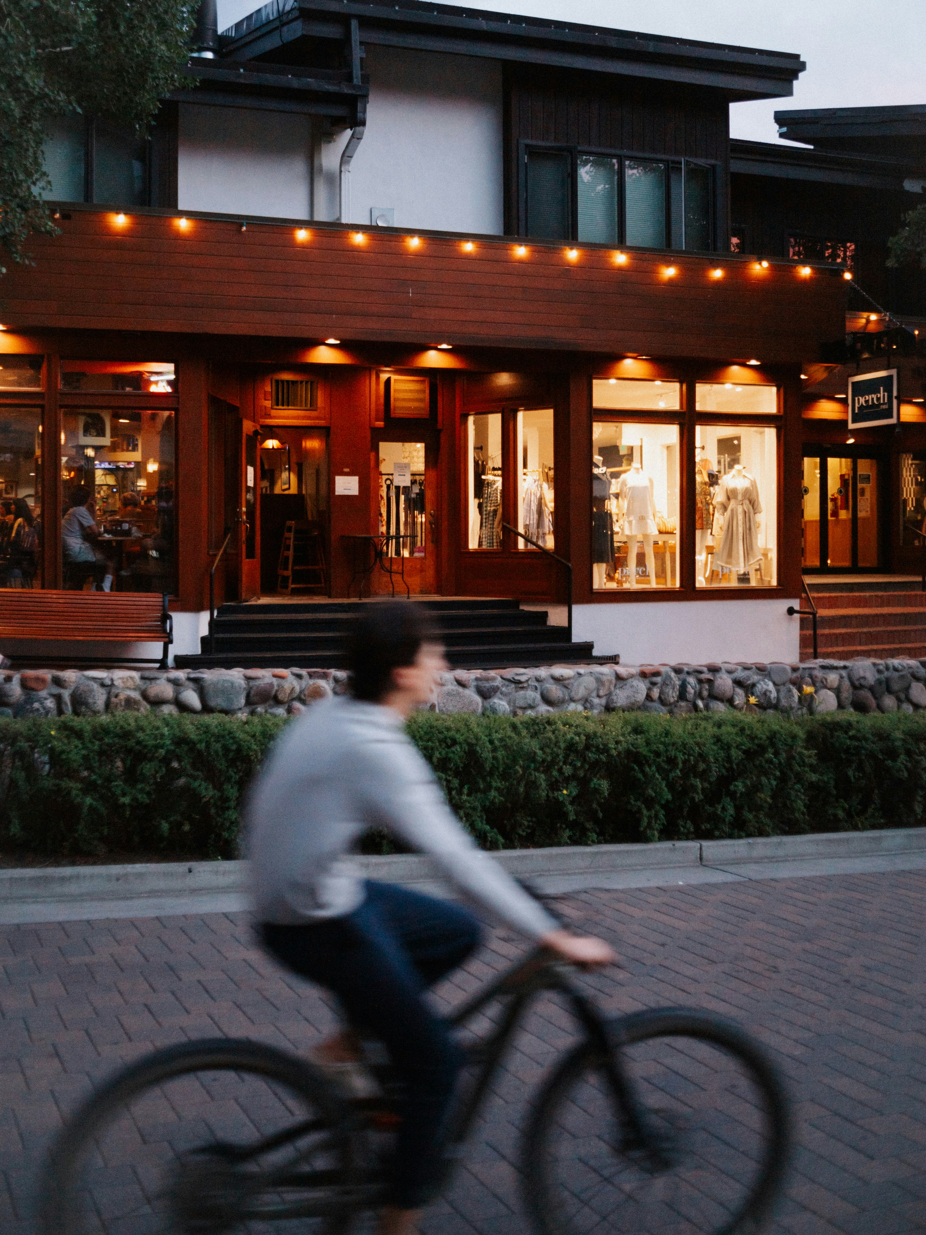 Person rides bicycle past illuminated building at dusk